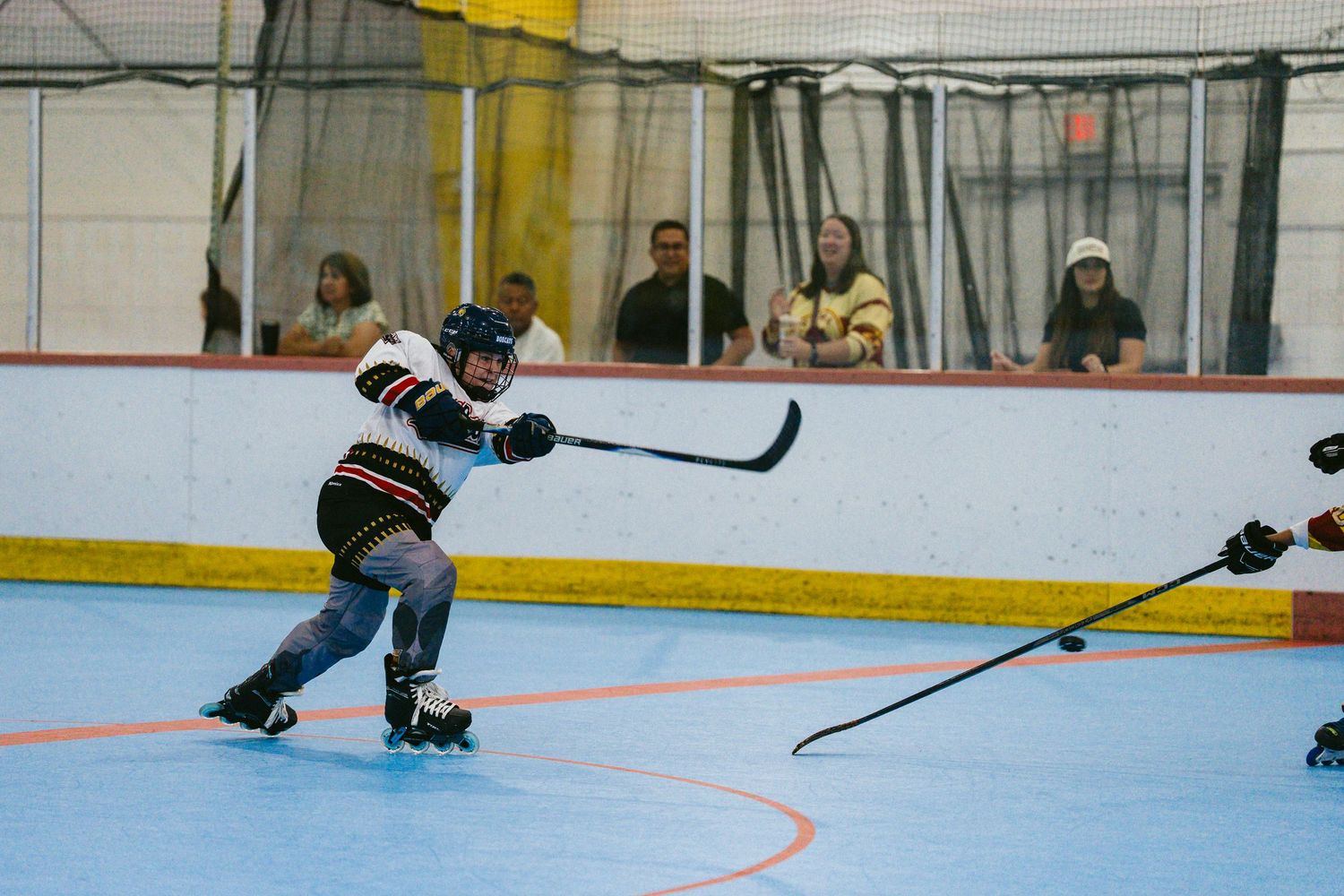 Young roller hockey player takes a shot on goal during an indoor inline hockey game with spectators watching.