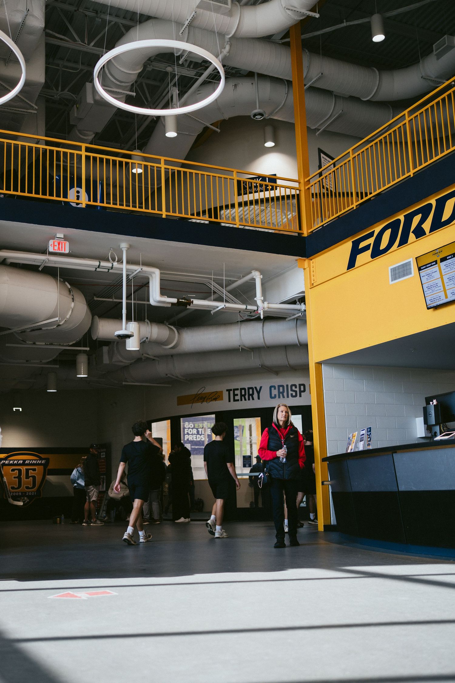 Modern hockey arena lobby with yellow accents, Terry Crisp signage, and Ford branding.