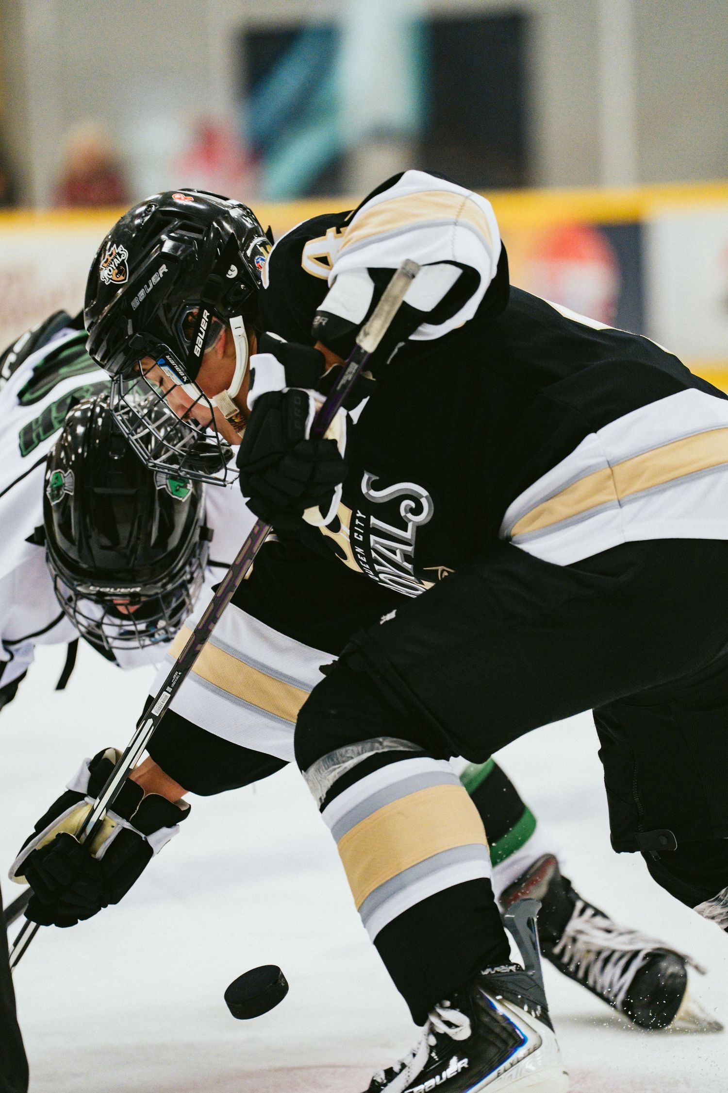 Two youth hockey players face off on the ice during a competitive game, wearing black helmets and jerseys.