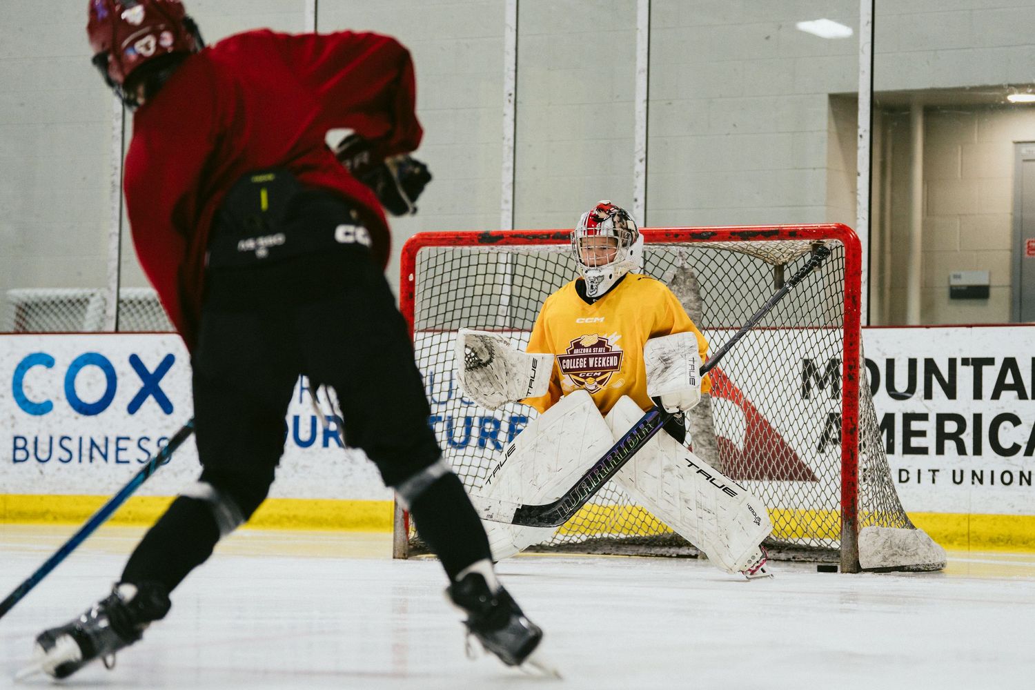 Youth hockey goalie in yellow gear prepares to make a save during an indoor practice session.