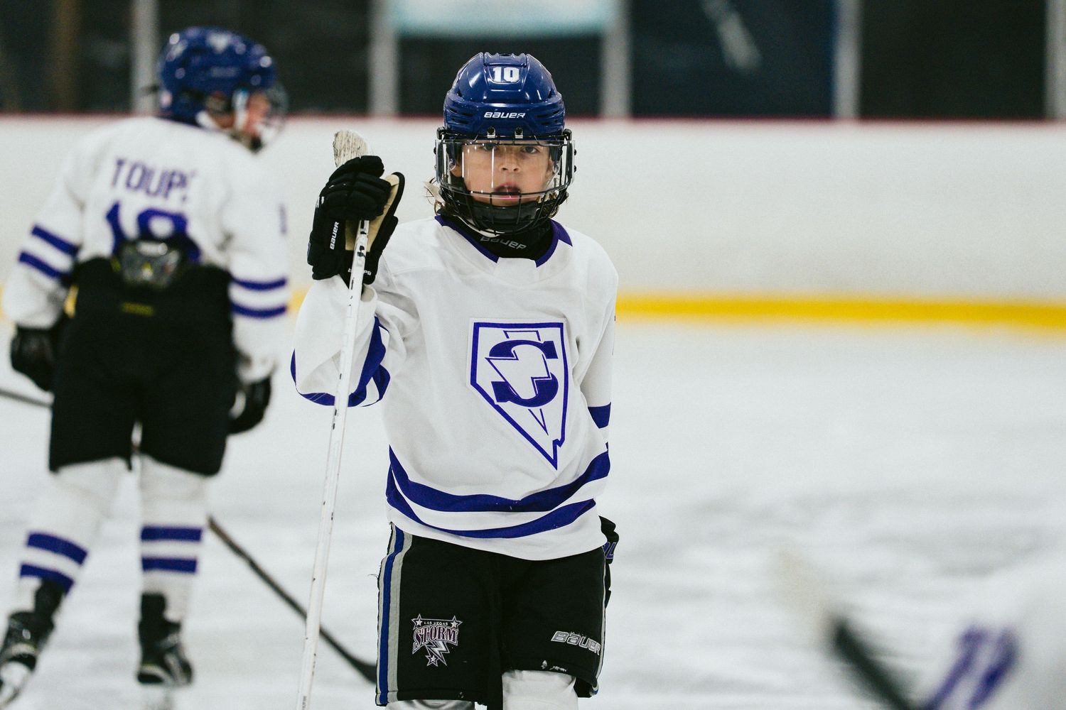 Hockey player in white and blue uniform skating with puck during competitive match.