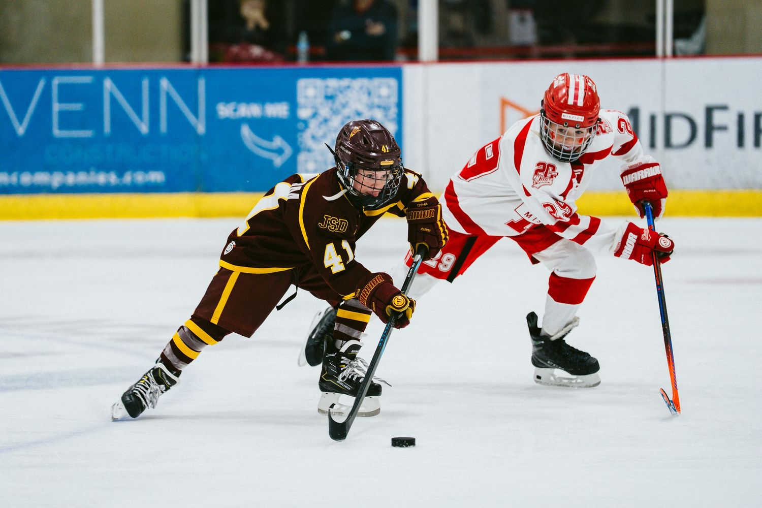 Hockey players battle for control of the puck near the boards during a competitive game.