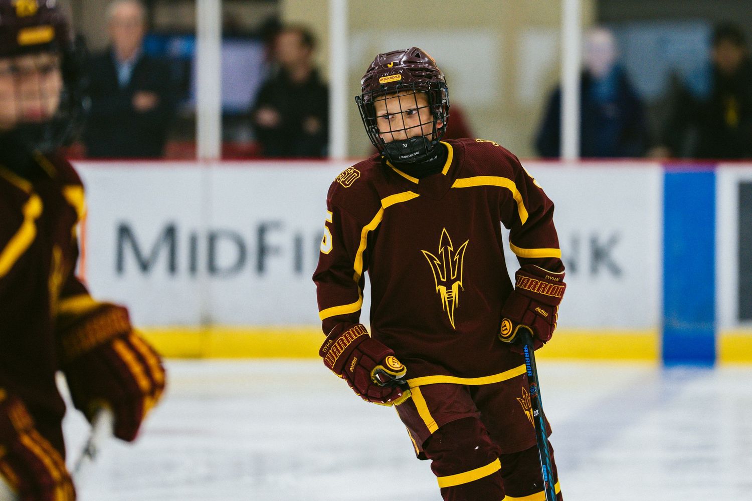 Ice hockey players in brown and gold jerseys compete against team in red during intense game.