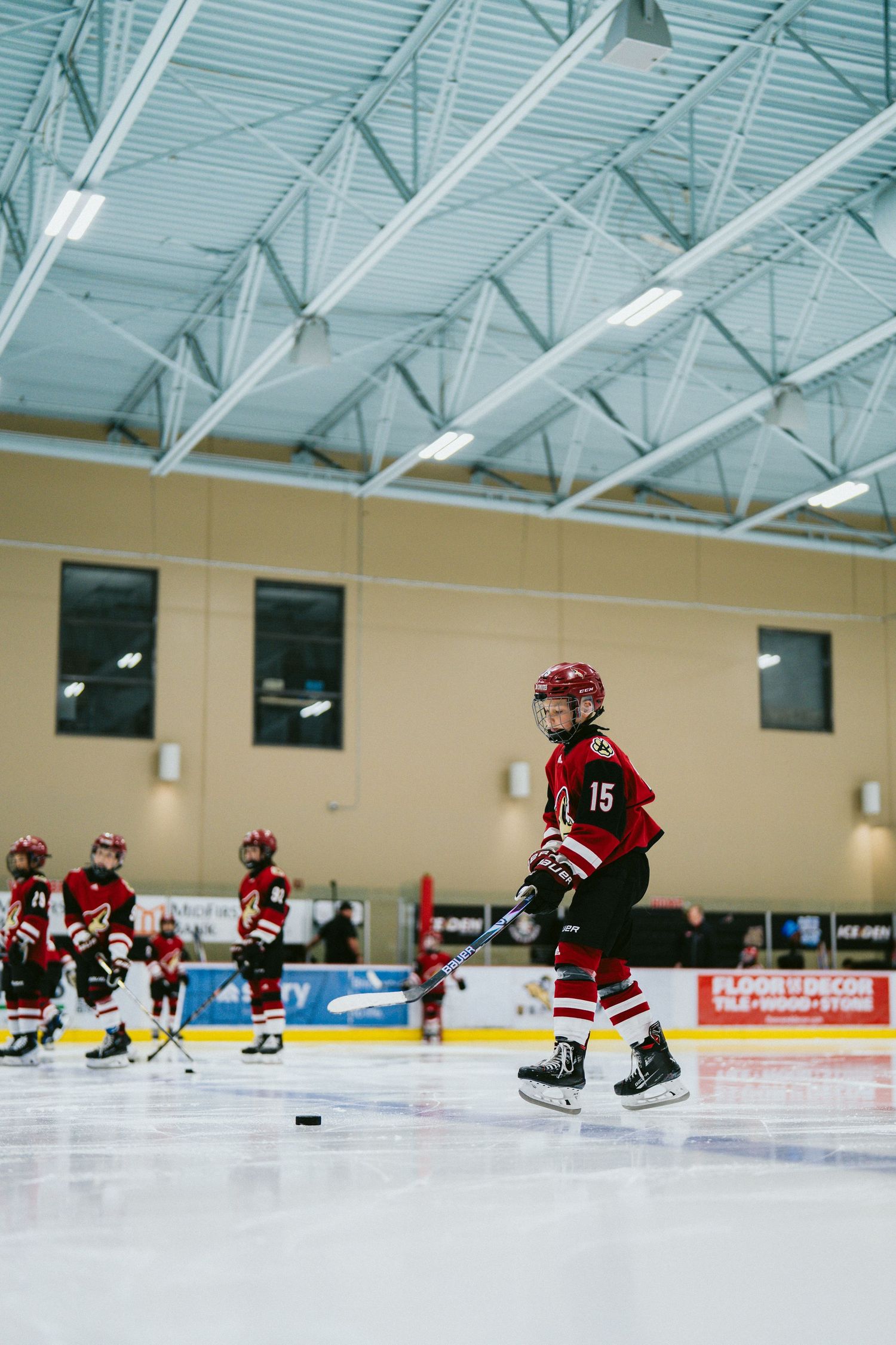 Young hockey player skates on ice rink under industrial ceiling lights during practice.