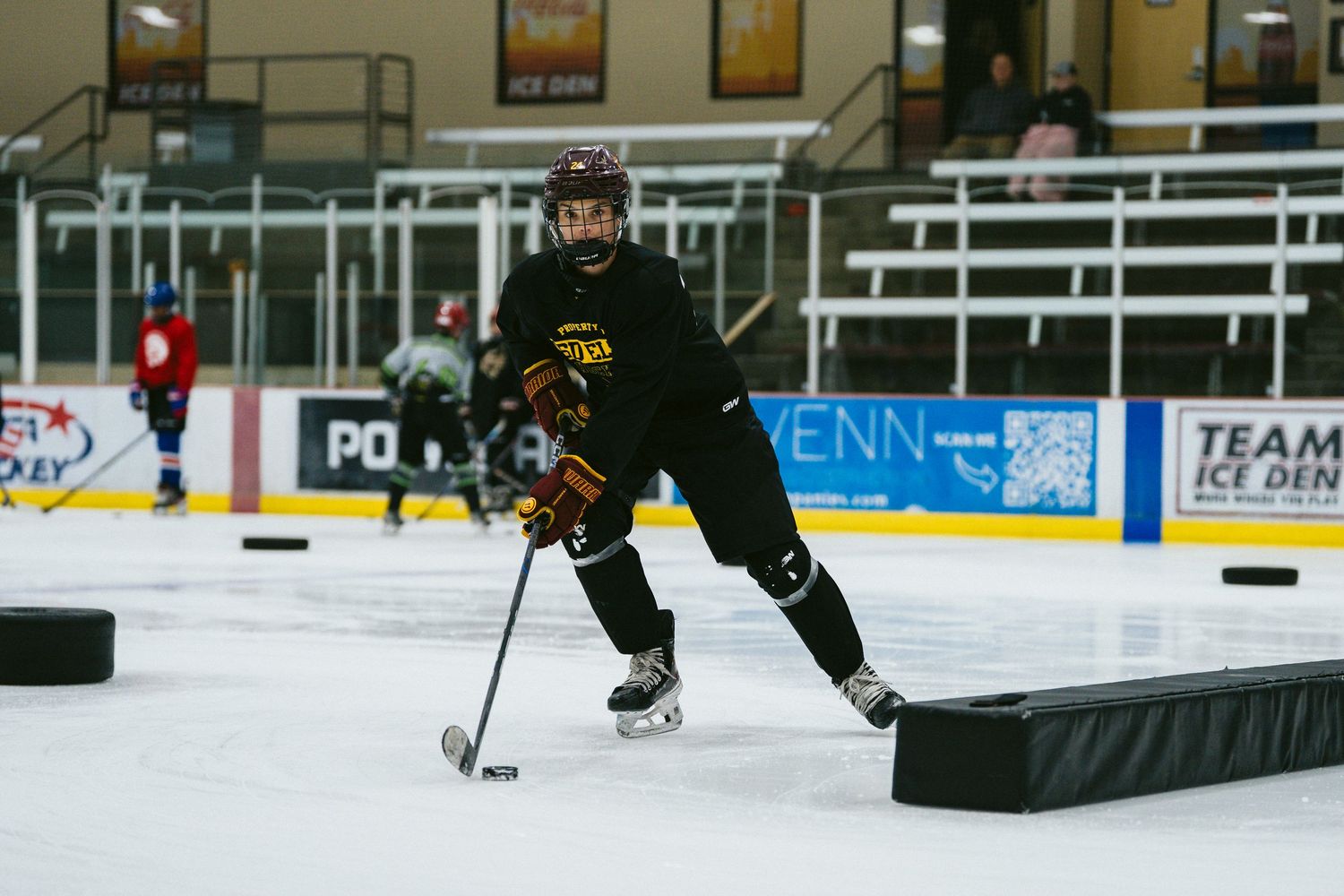 Hockey player in black uniform skating with puck during ice hockey practice at indoor rink.