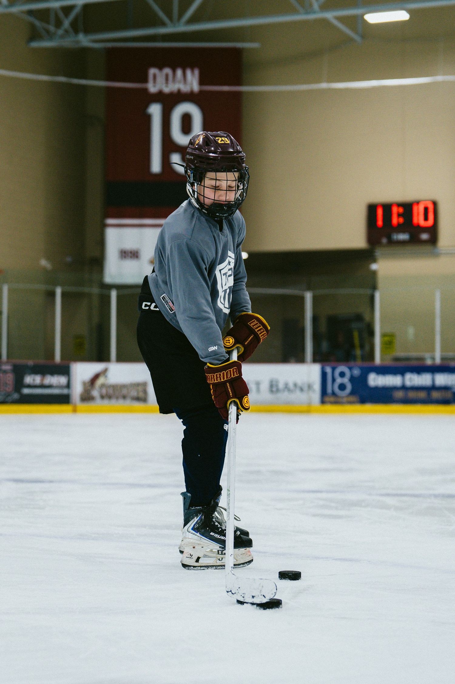 Young hockey player in full gear practices puck handling on indoor ice rink with number 19 Doan jersey retired in background.