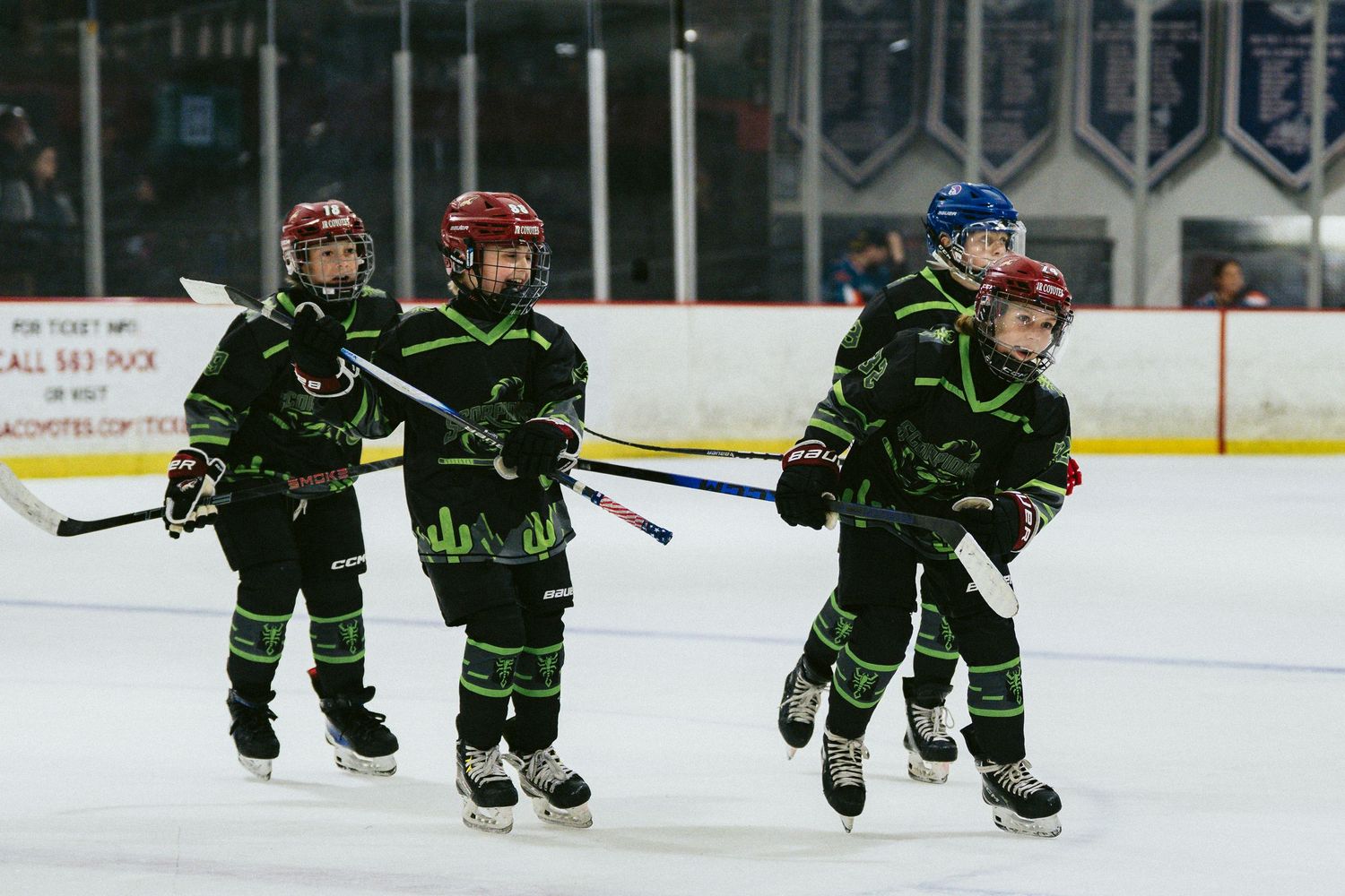 Group of young hockey players in matching black green uniforms skating together on ice rink.