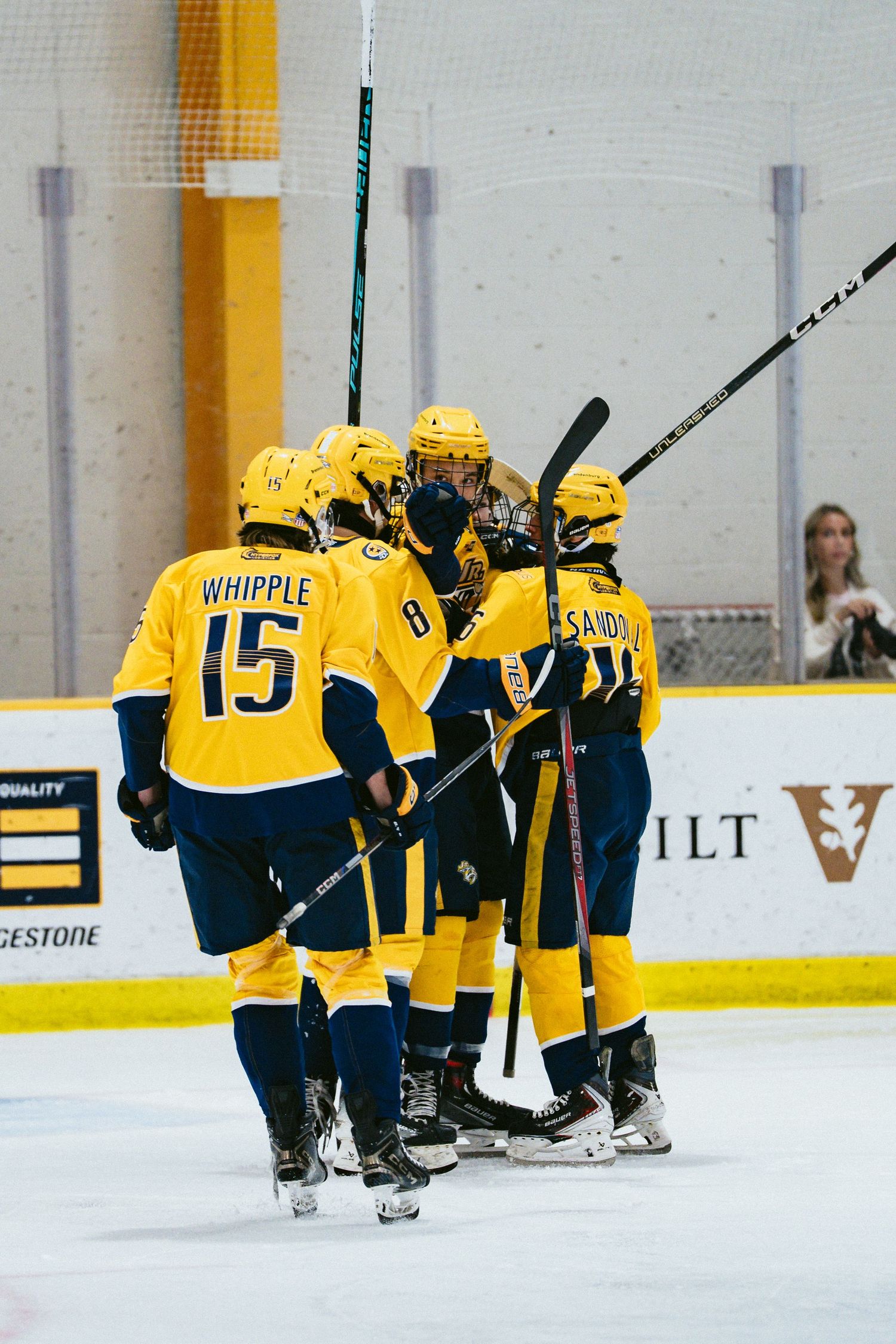 Yellow-uniformed hockey players including Whipple number 15 celebrate a goal on the ice.
