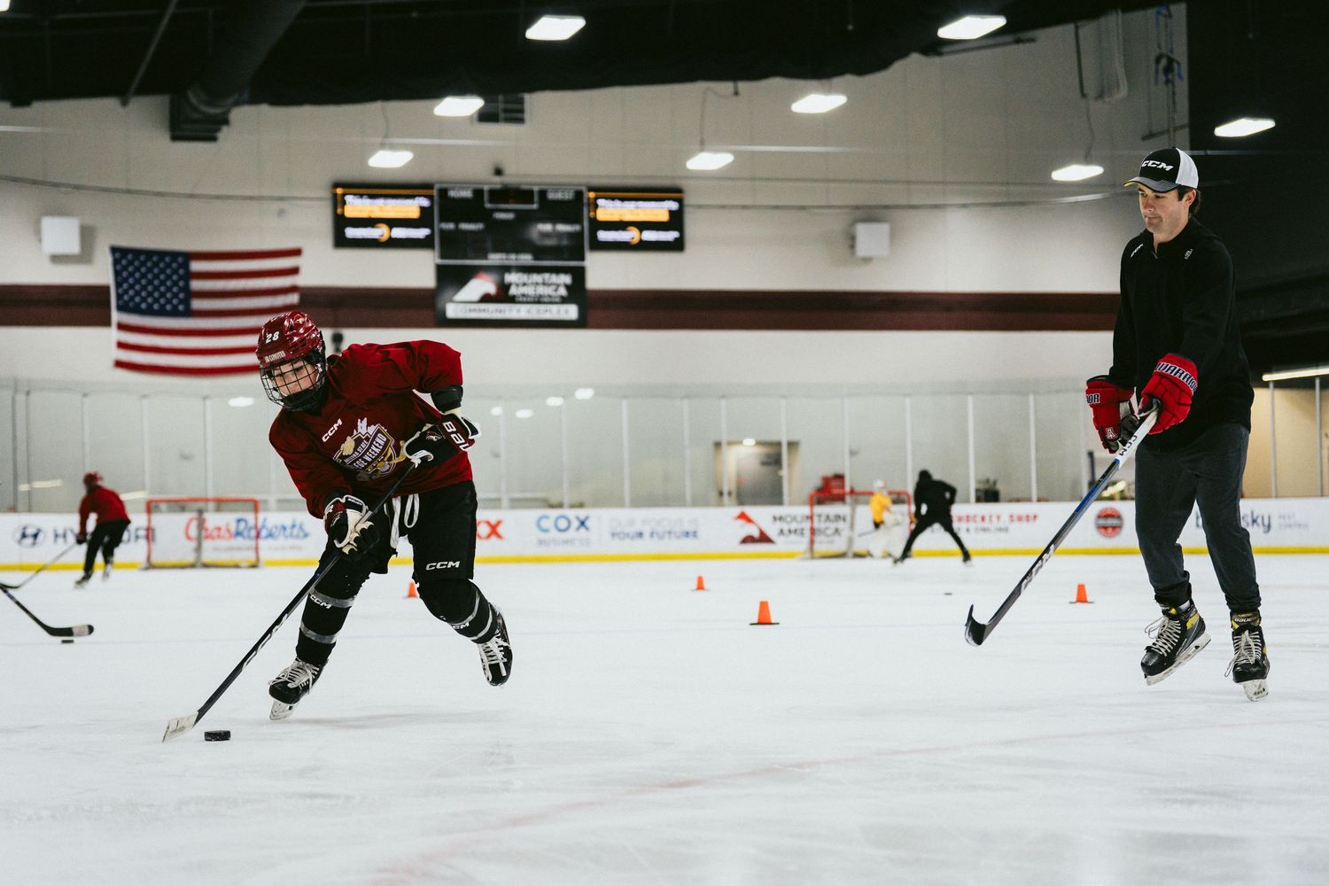 Young hockey player practices skating drills with a coach on an indoor ice rink during training.