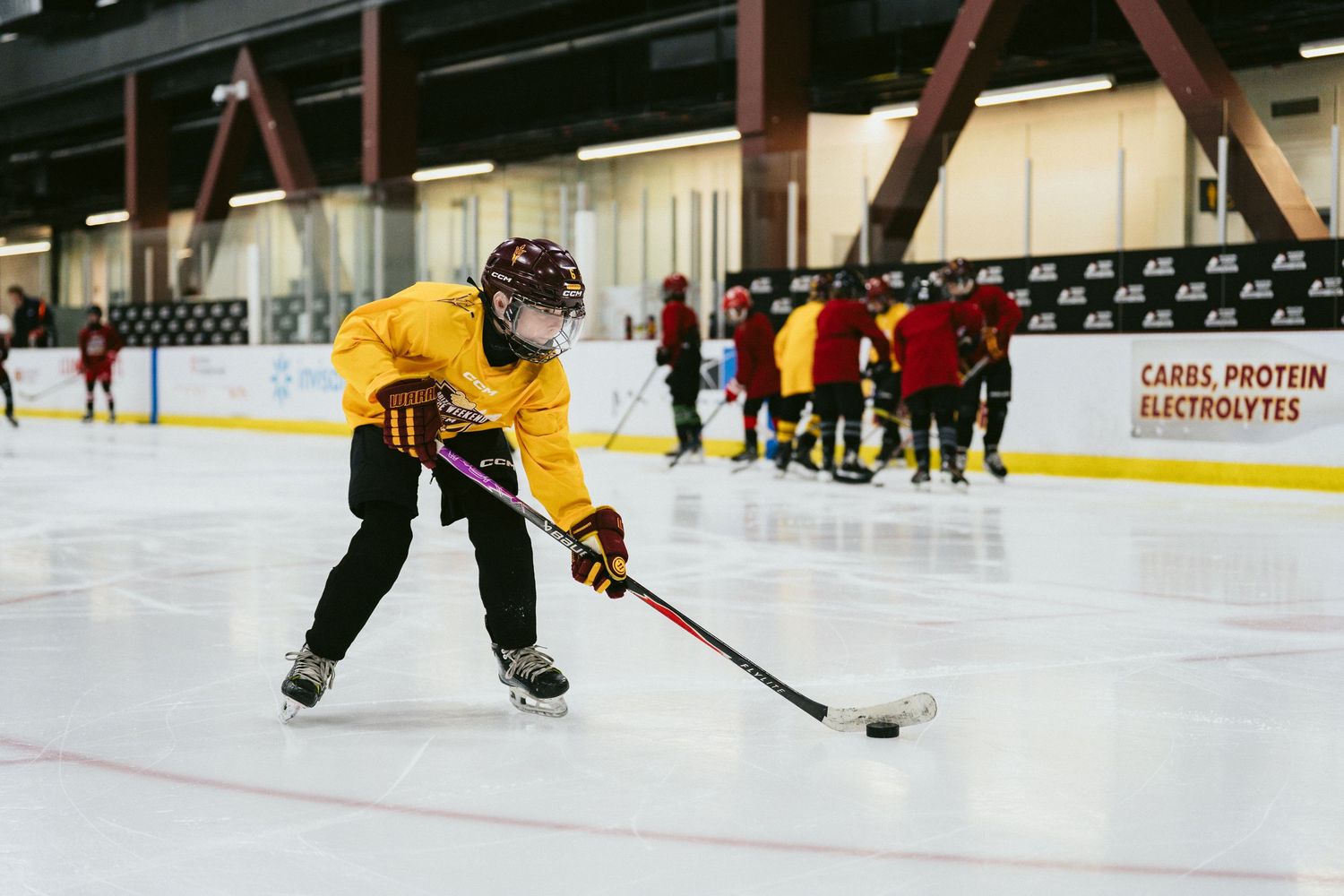 Young hockey player in yellow jersey handling puck during indoor ice hockey practice drill.