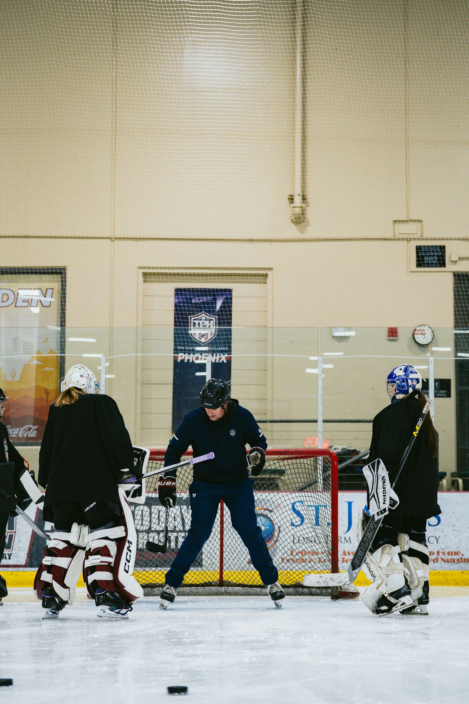 Hockey coach demonstrates technique to two goaltenders during indoor ice rink training session in Phoenix.