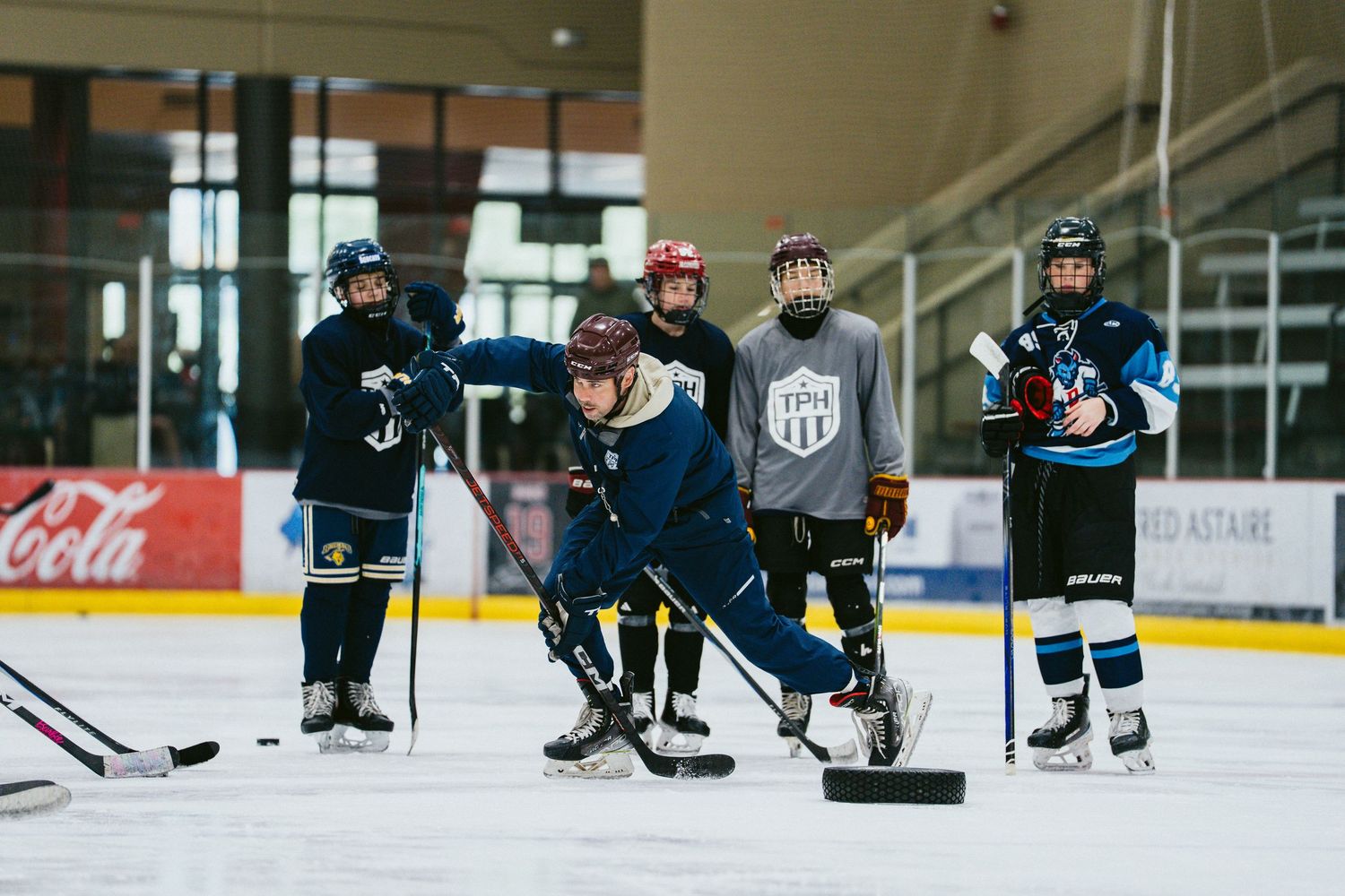 Young hockey players practice drills on indoor ice rink during TPH hockey training session.