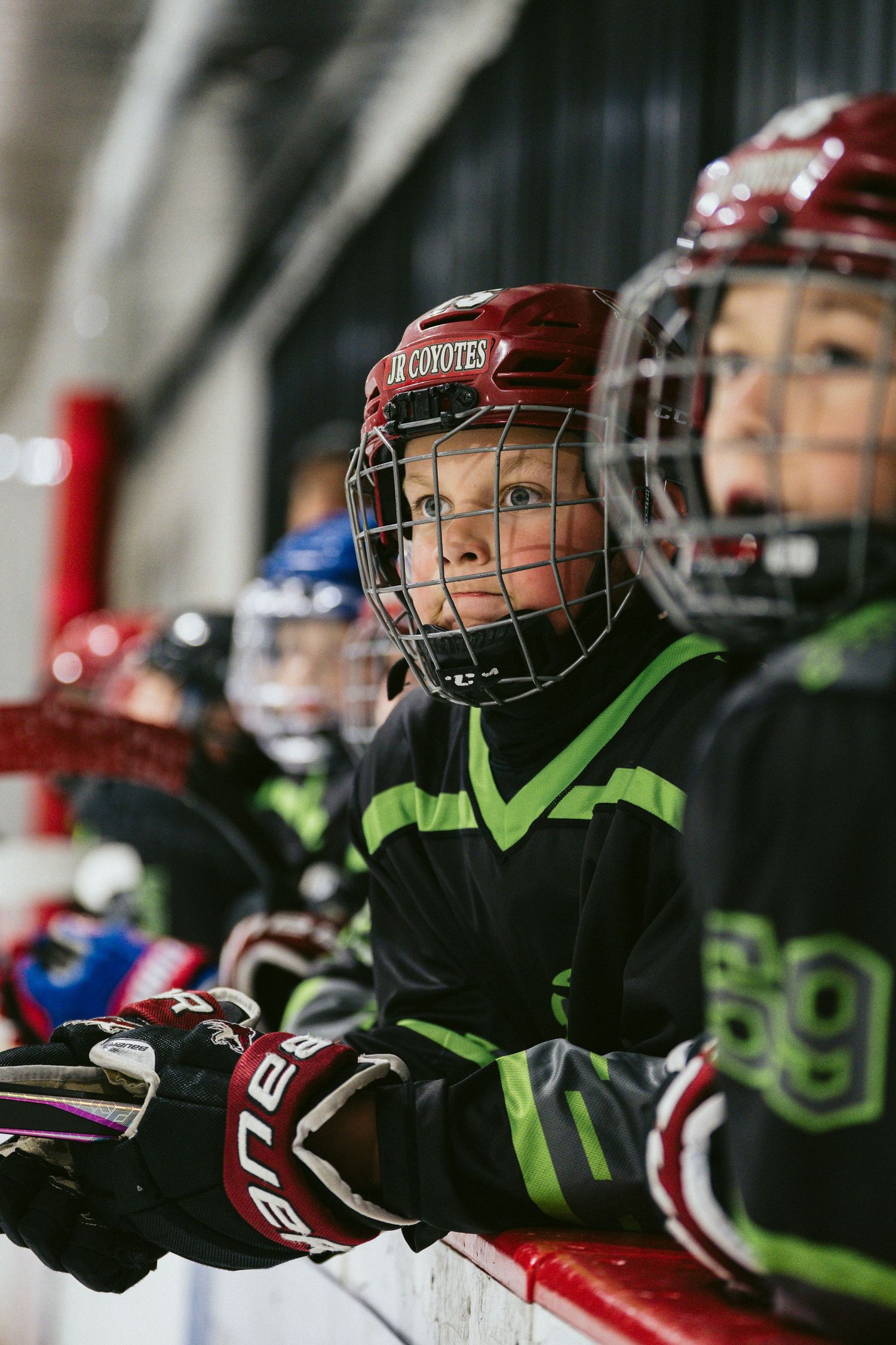 Young ice hockey players in red helmets and black uniforms wait on bench during youth hockey game.