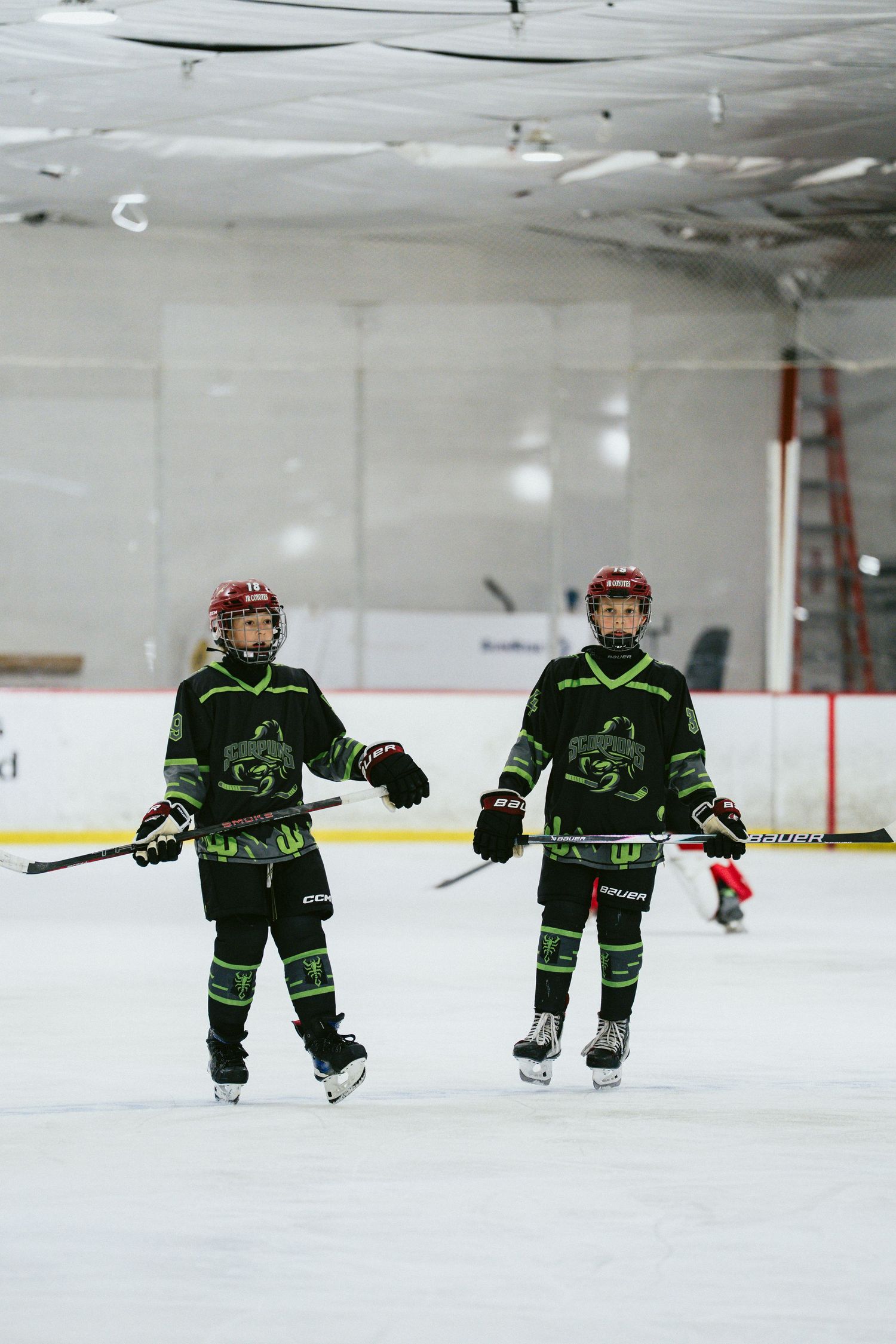 Two young hockey players in matching black and green uniforms skate together on an indoor ice rink.