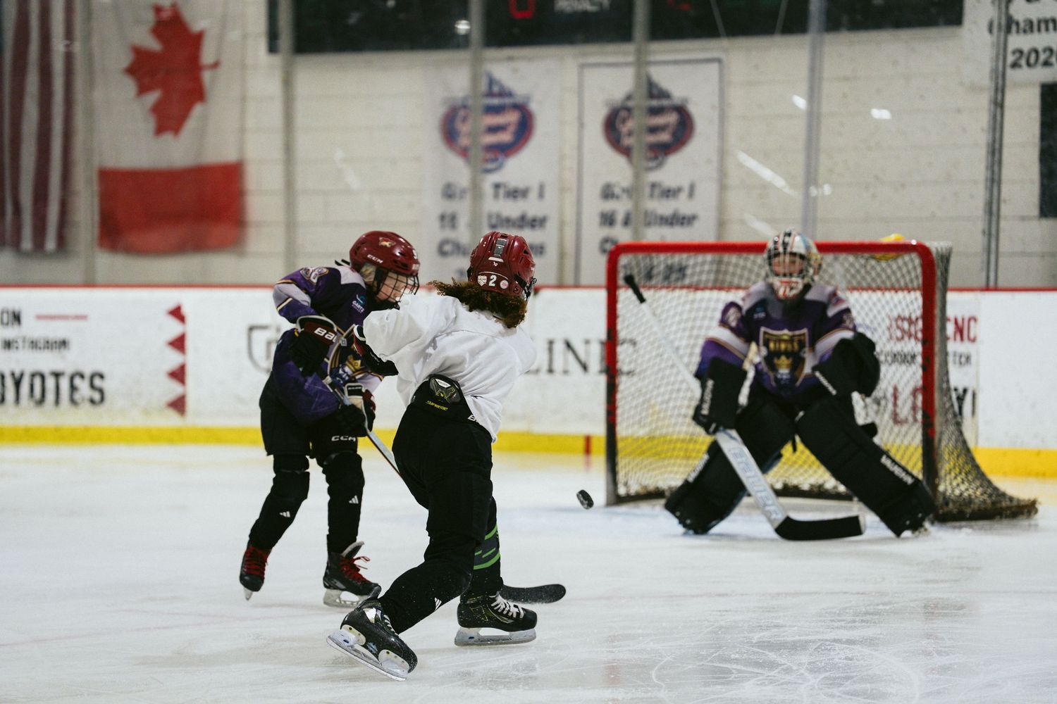 Youth hockey players compete near the goal as goalie defends during an indoor ice hockey game.