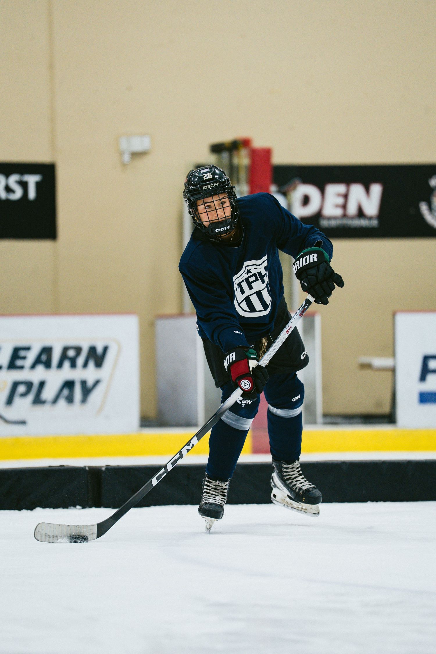 Young hockey player in dark navy jersey skates with the puck during an indoor ice rink practice session.