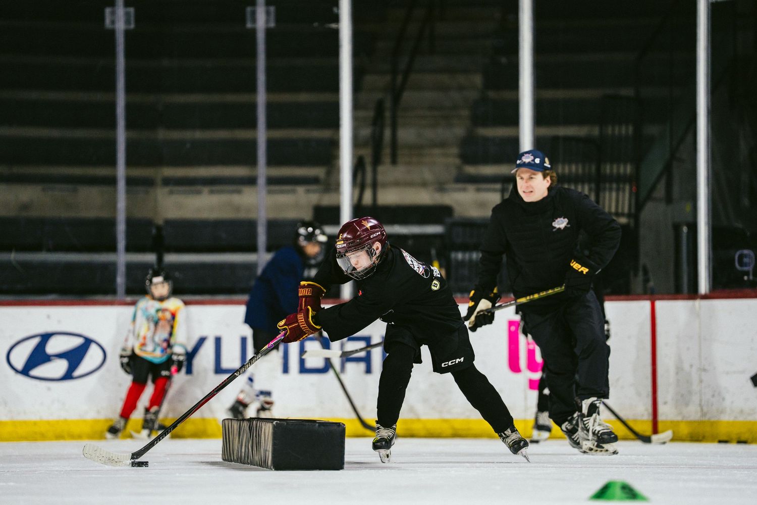 Youth hockey players practicing puck handling drills with a coach on indoor ice rink.