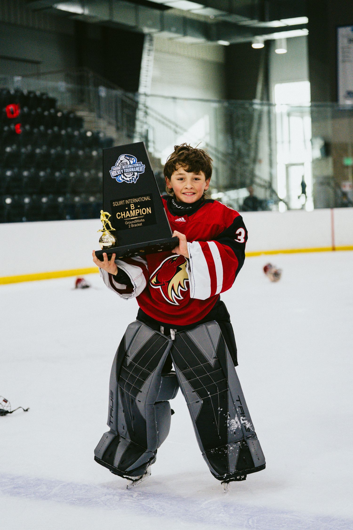 Young hockey goalies practicing on ice rink in red and black uniforms.