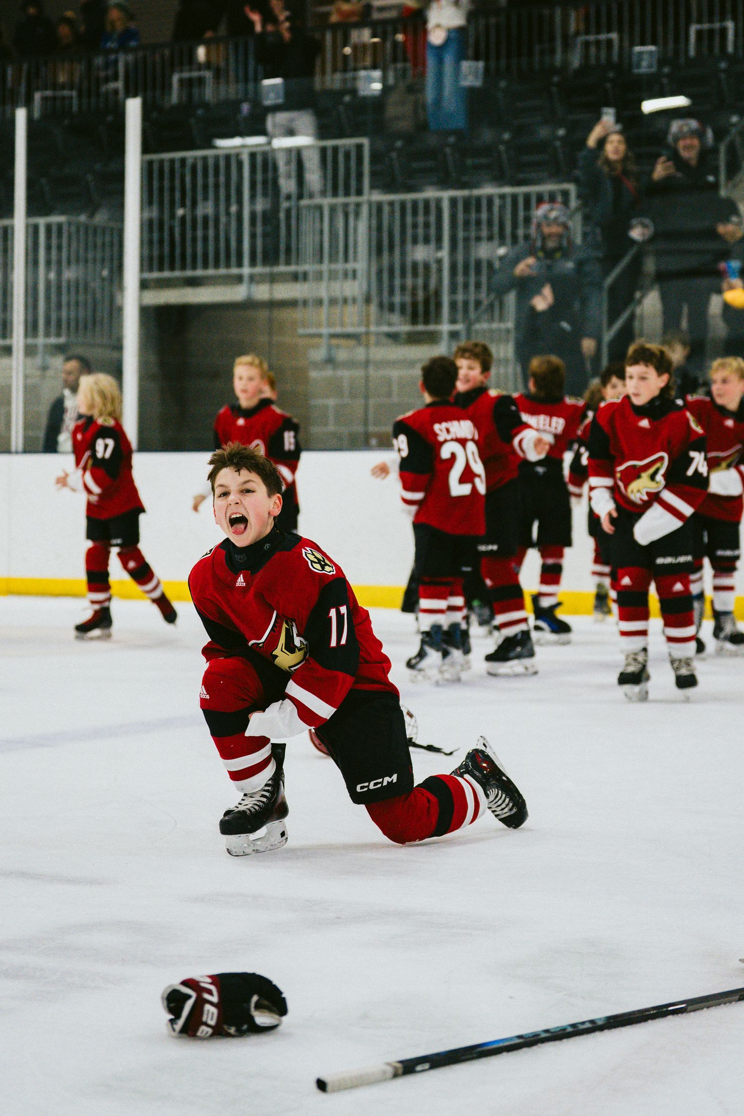 Youth hockey players in red jerseys sliding on ice during a fun team drill at an indoor rink.