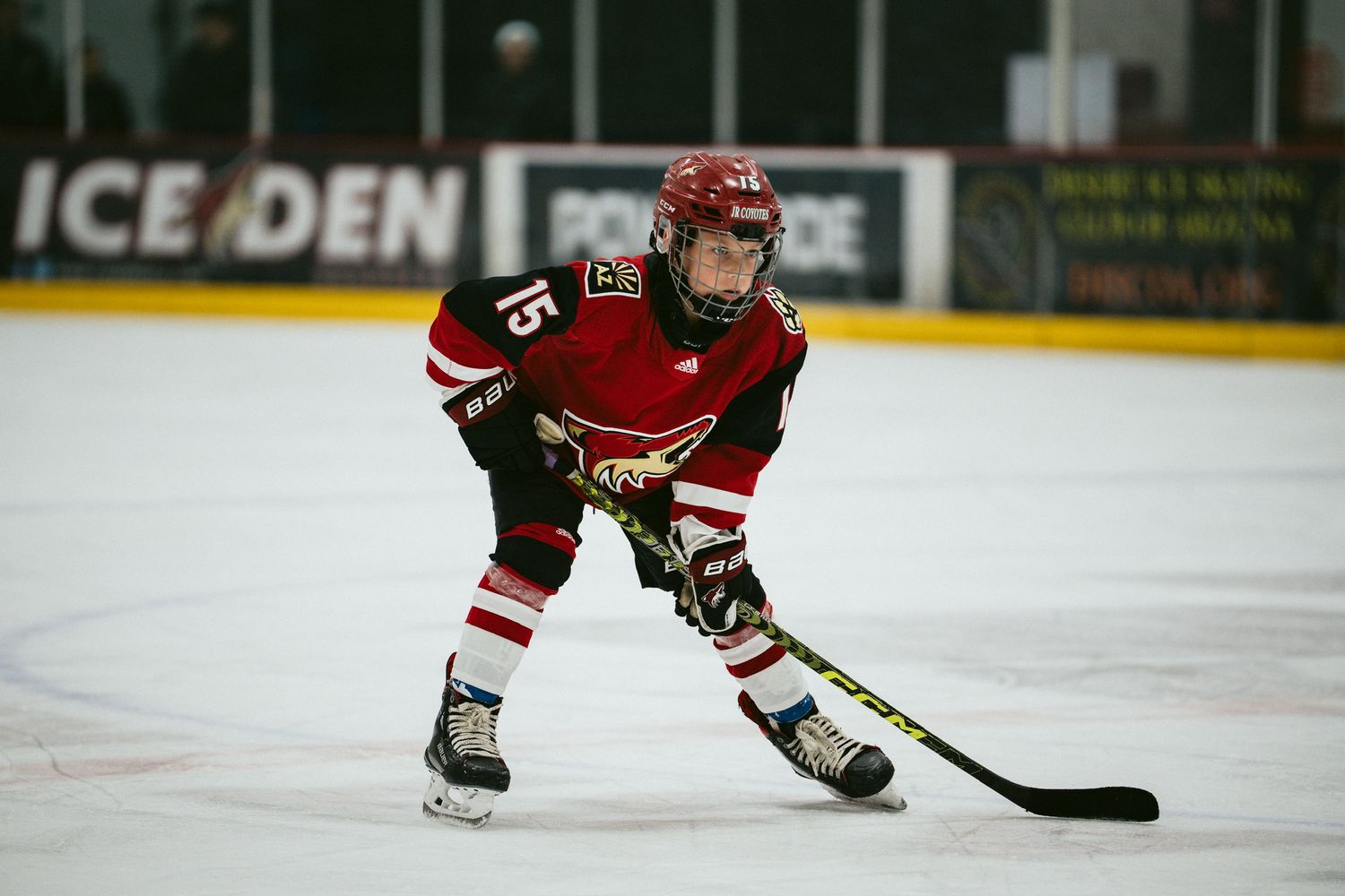 Youth hockey player in red jersey skates with the puck during a game.