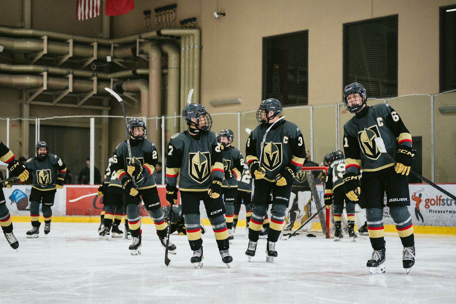 Hockey players in black and gold uniforms spread across the ice during team practice.