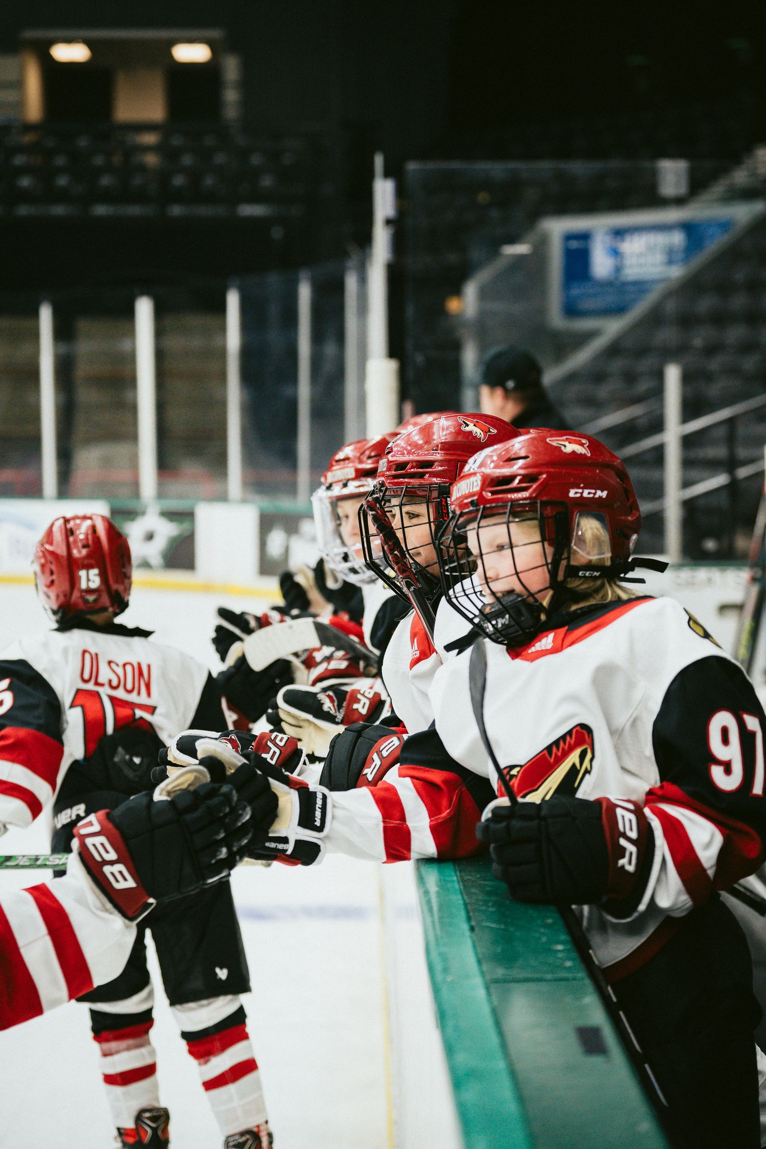 Hockey team lined up along the boards during practice wearing red and white uniforms.