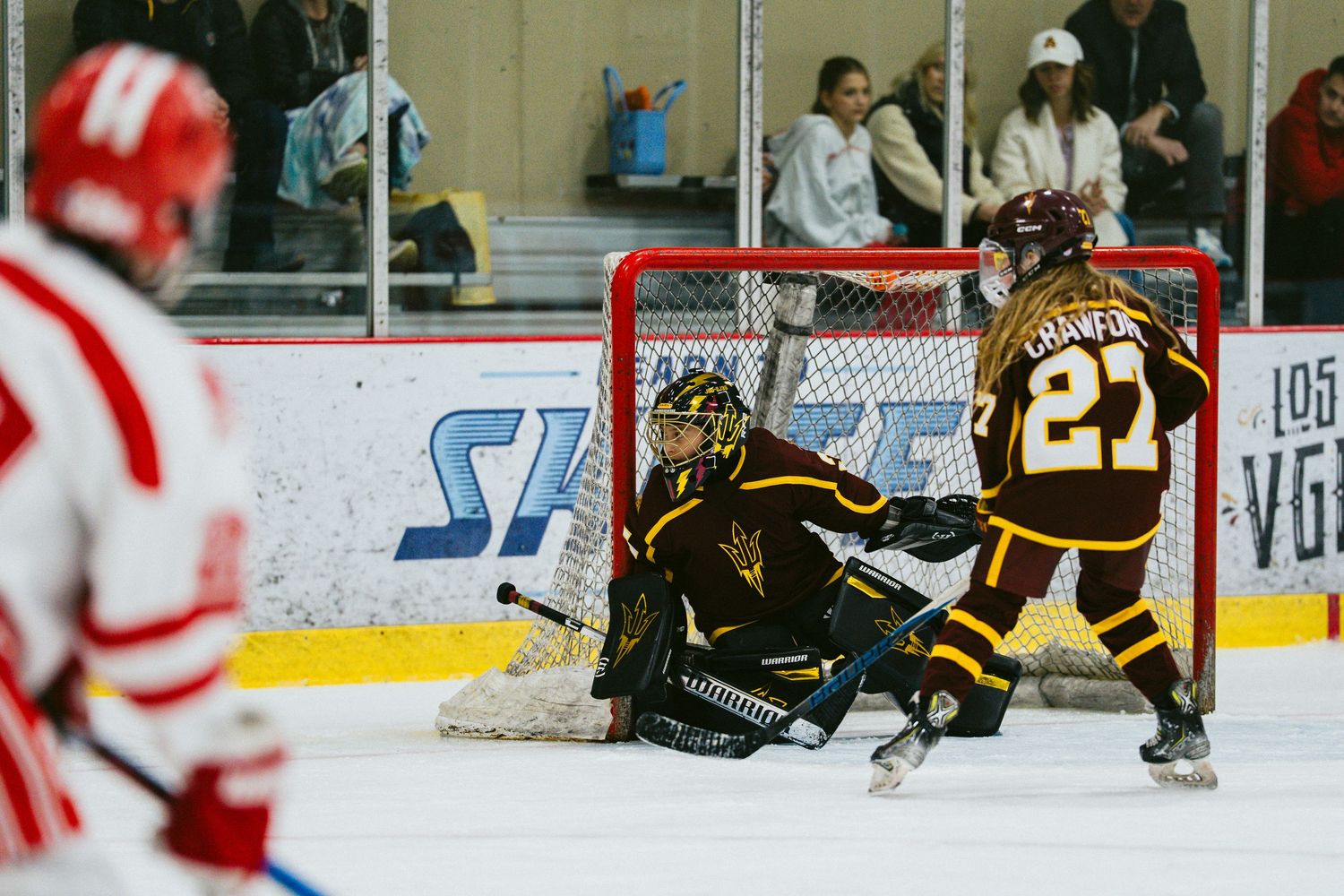 Hockey players in brown and red jerseys compete for the puck during an intense ice hockey match.