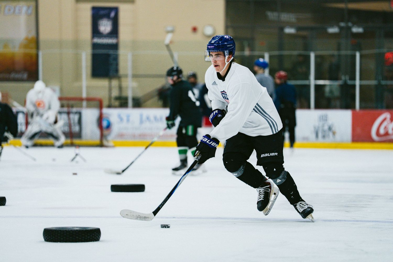 Hockey player in white jersey handles puck during indoor ice rink practice session.