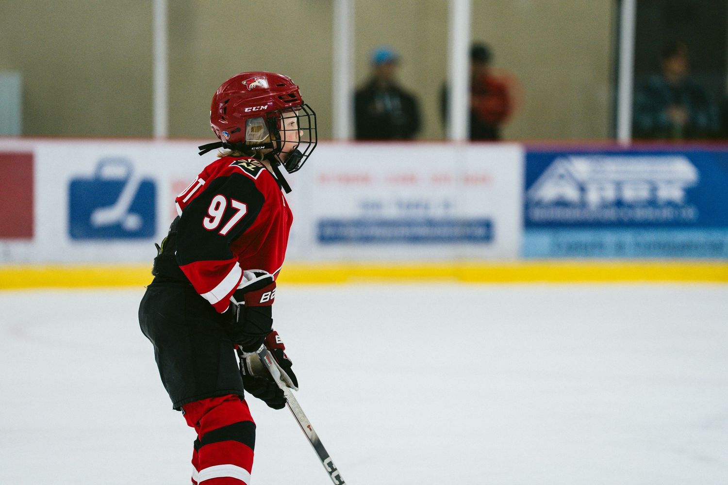 Youth hockey player in red jersey and helmet skating on ice during game.