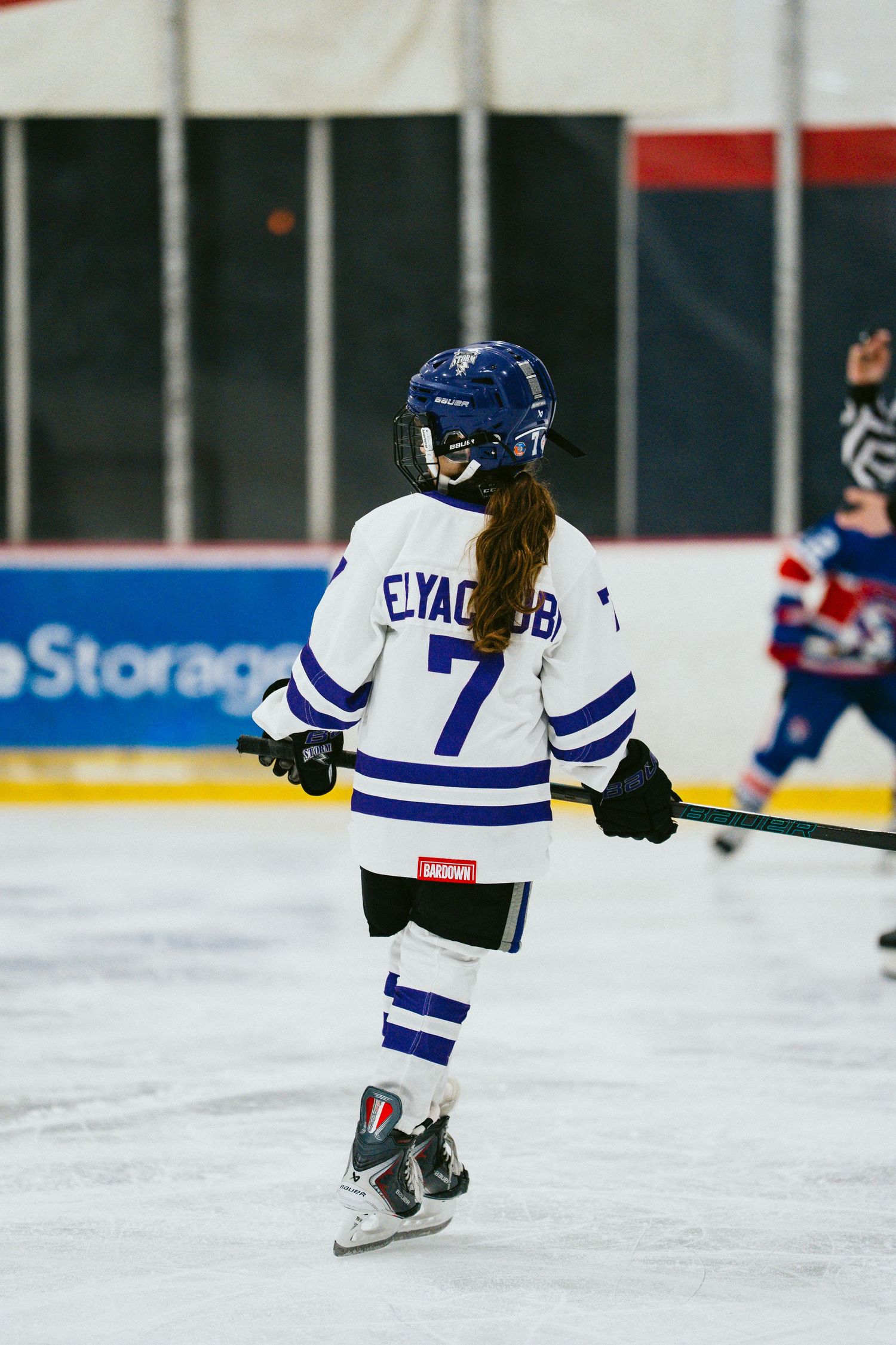 Young hockey player in blue and white striped jersey number 7 skating on ice rink during game.