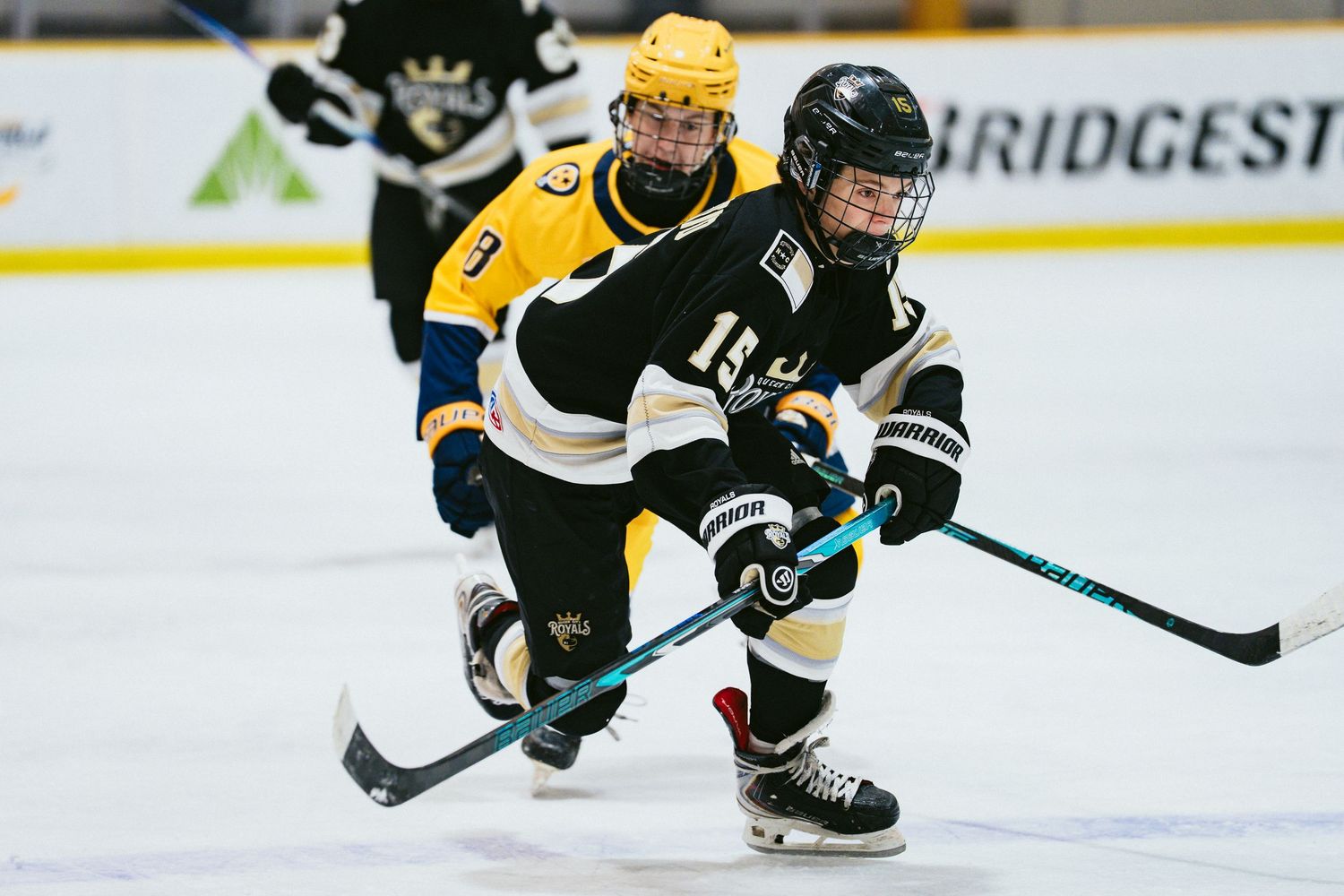 Two youth hockey players battle for the puck on the ice during a competitive youth hockey game at an indoor rink.