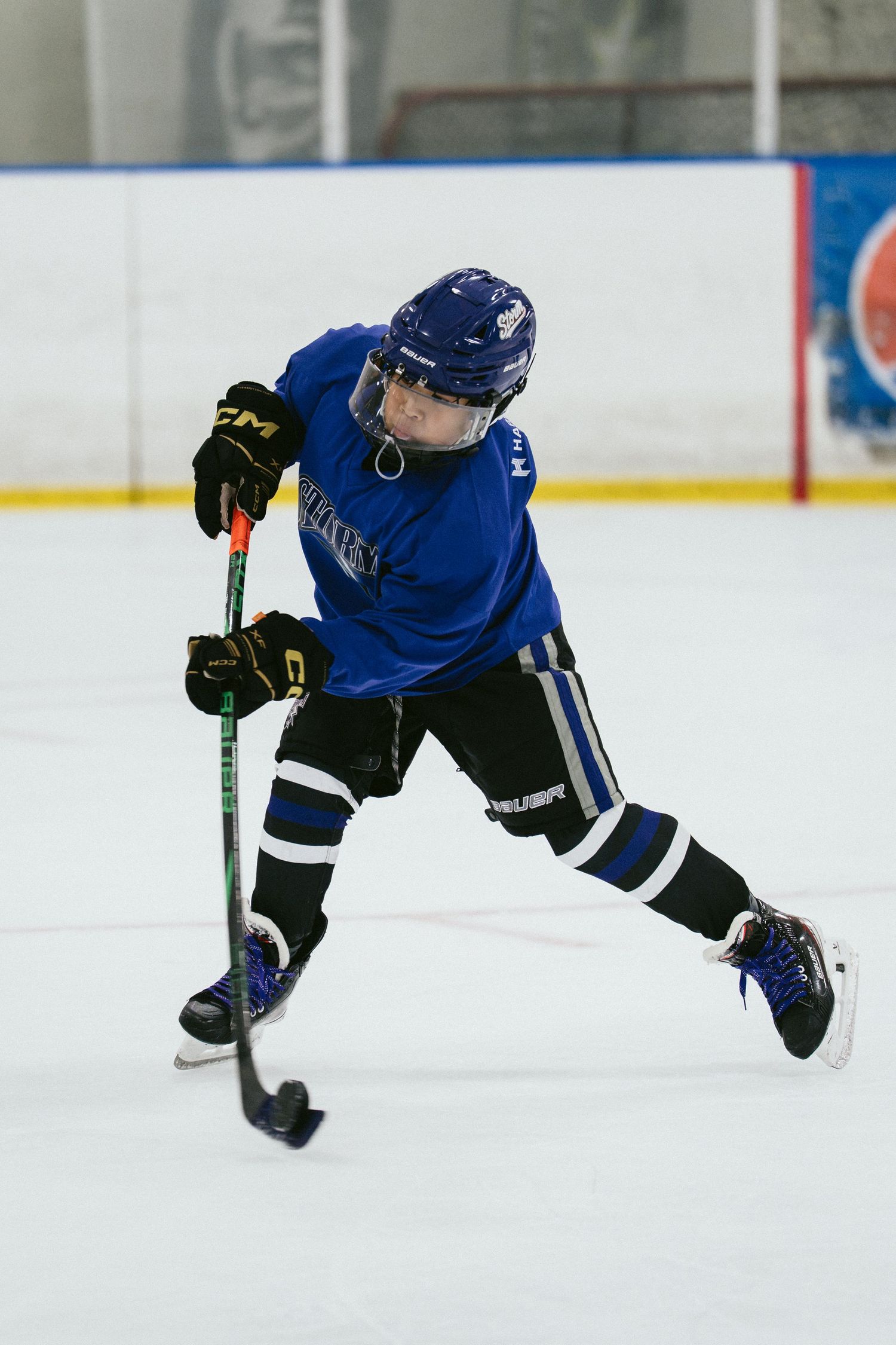 Young hockey player in blue uniform takes a shot on ice during youth hockey game.