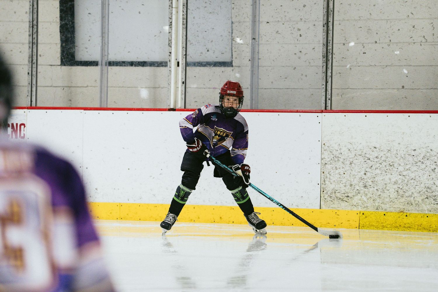 Youth hockey player in purple jersey controls the puck along the ice during a game.