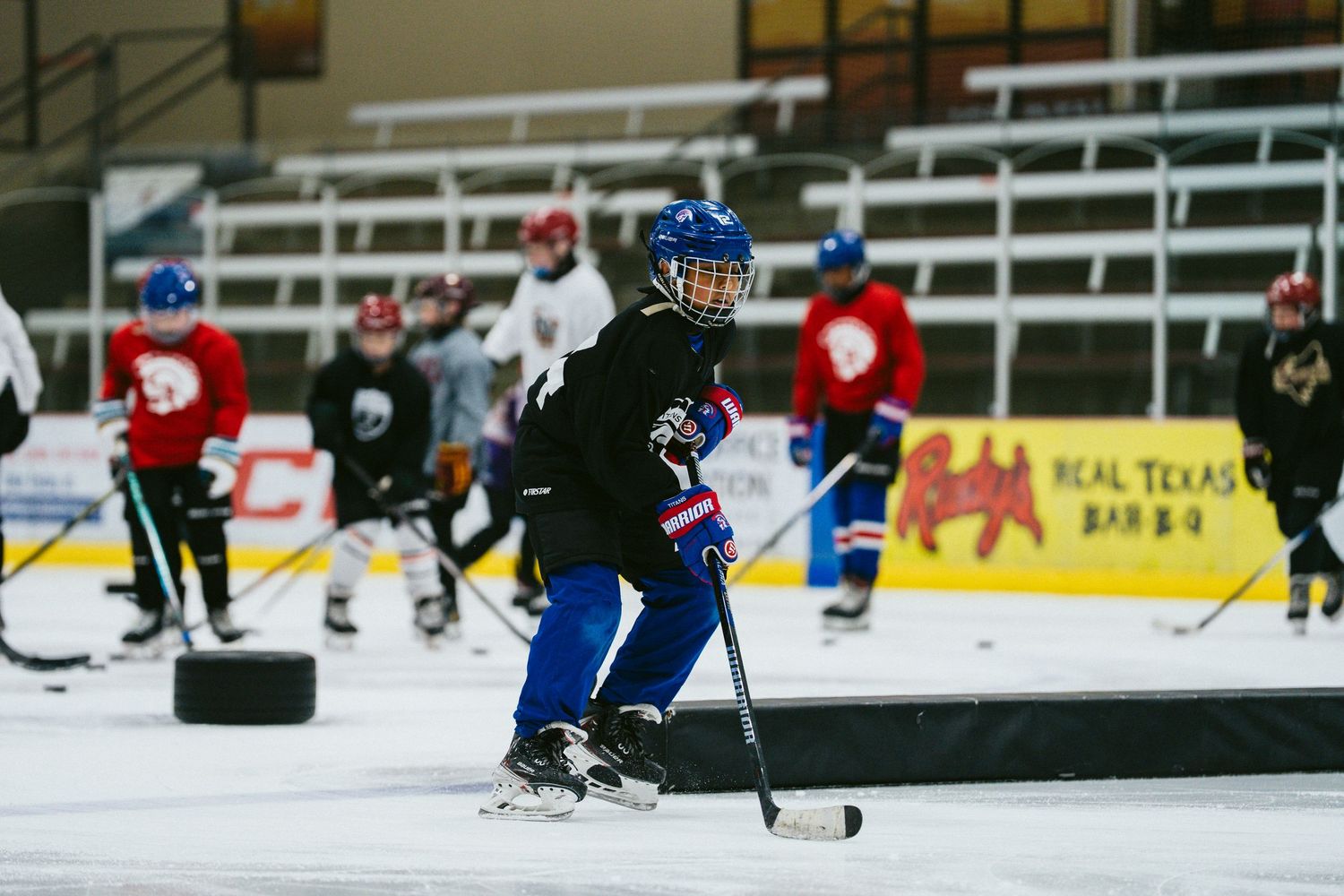 Young hockey player in blue helmet skating with puck during youth ice hockey practice session.