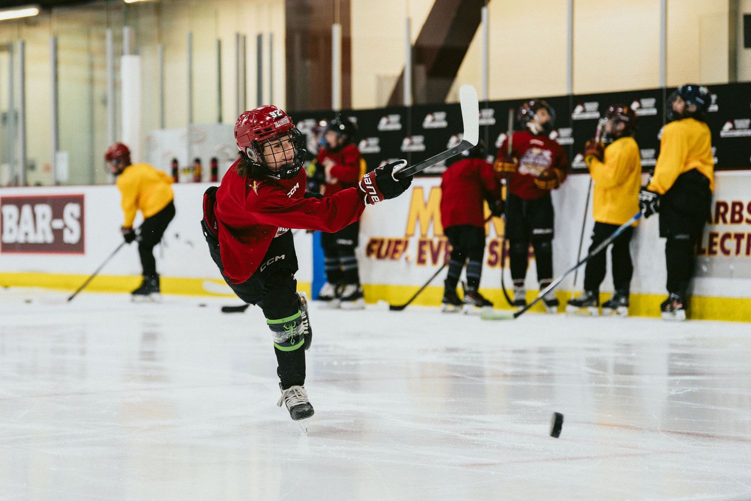 Youth hockey player in red jersey takes a powerful shot on ice during indoor hockey training.
