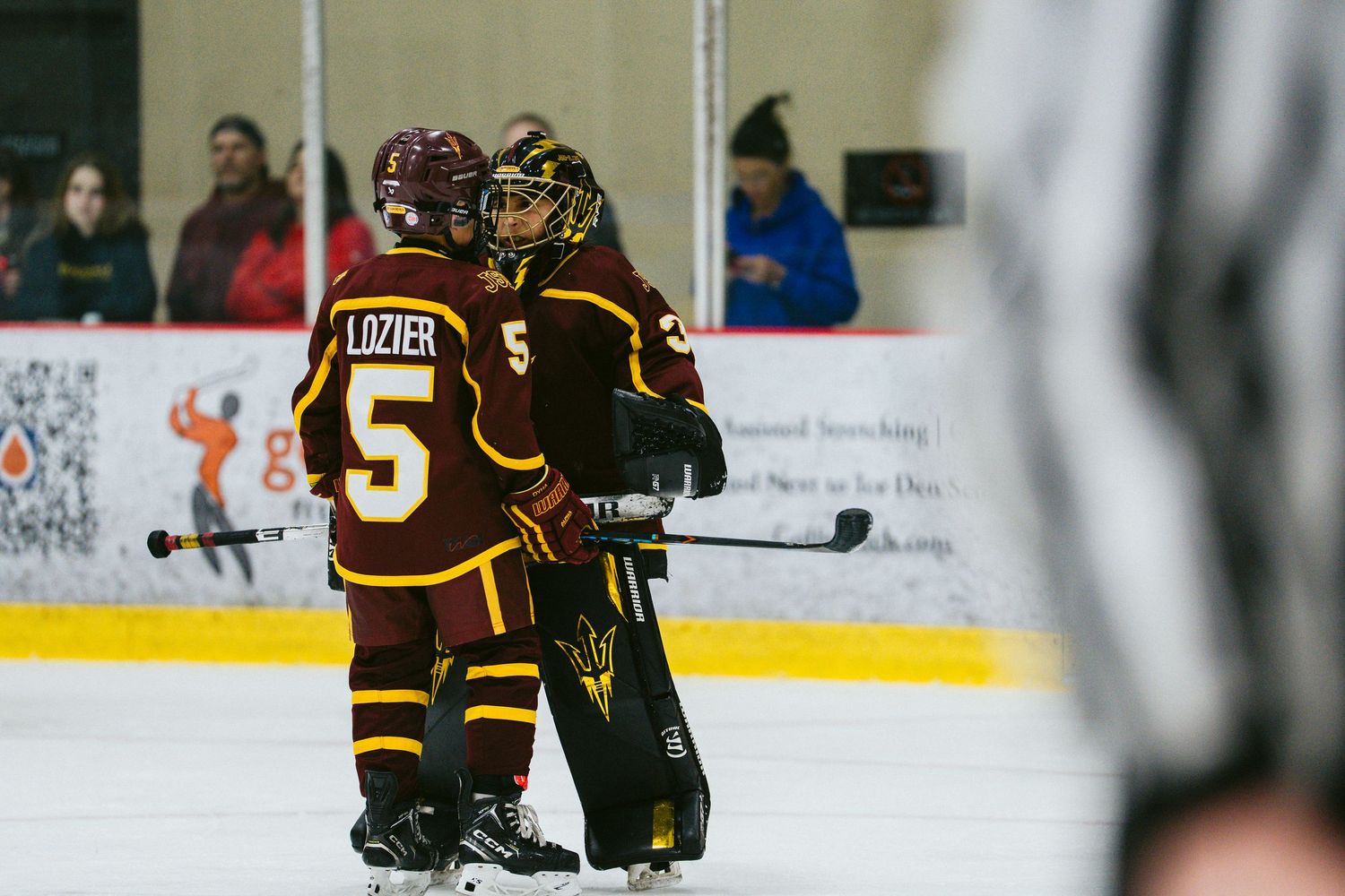 Hockey players in dark uniforms maneuver on the ice during an indoor match.