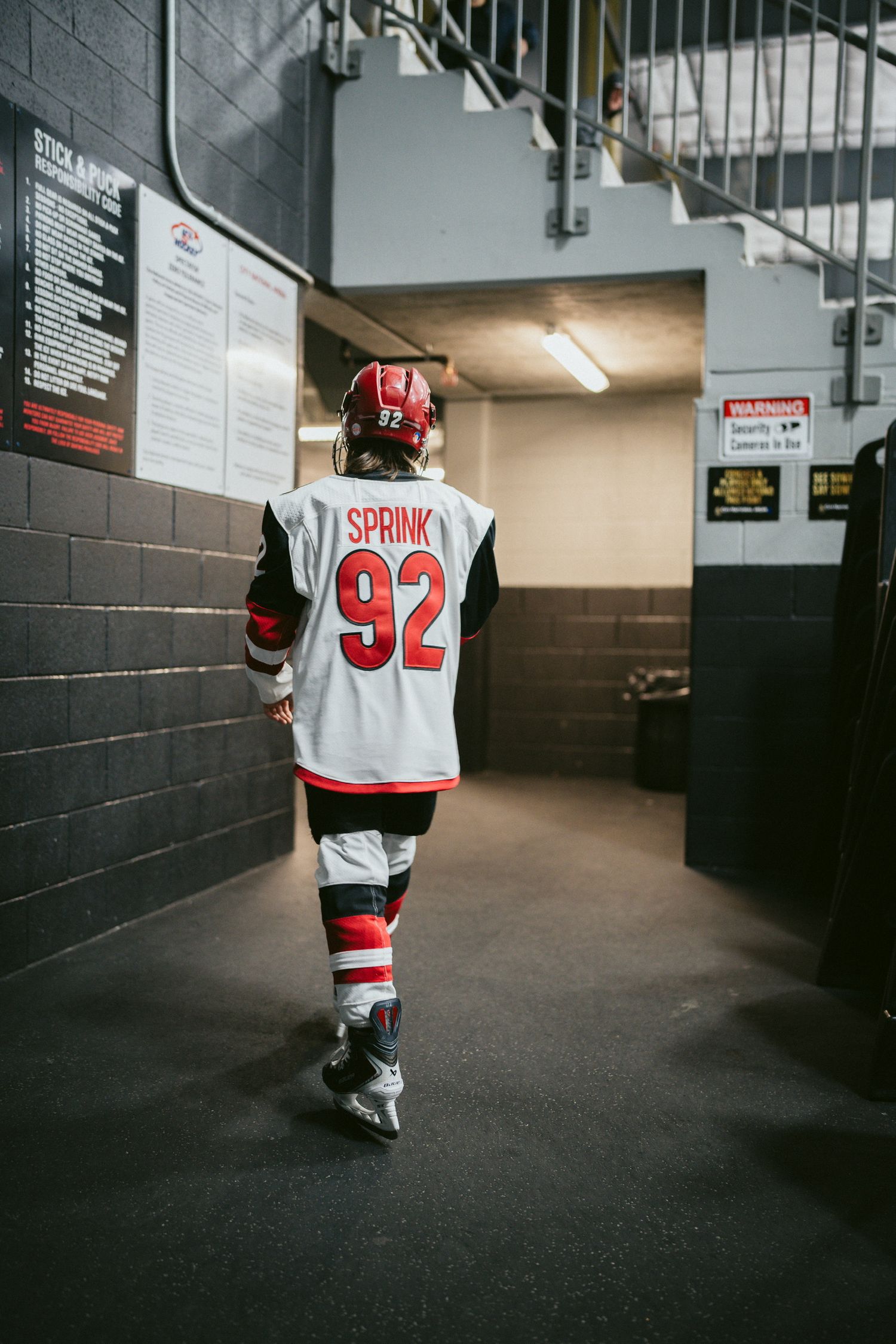 Hockey player wearing jersey number 92 walks down arena hallway.