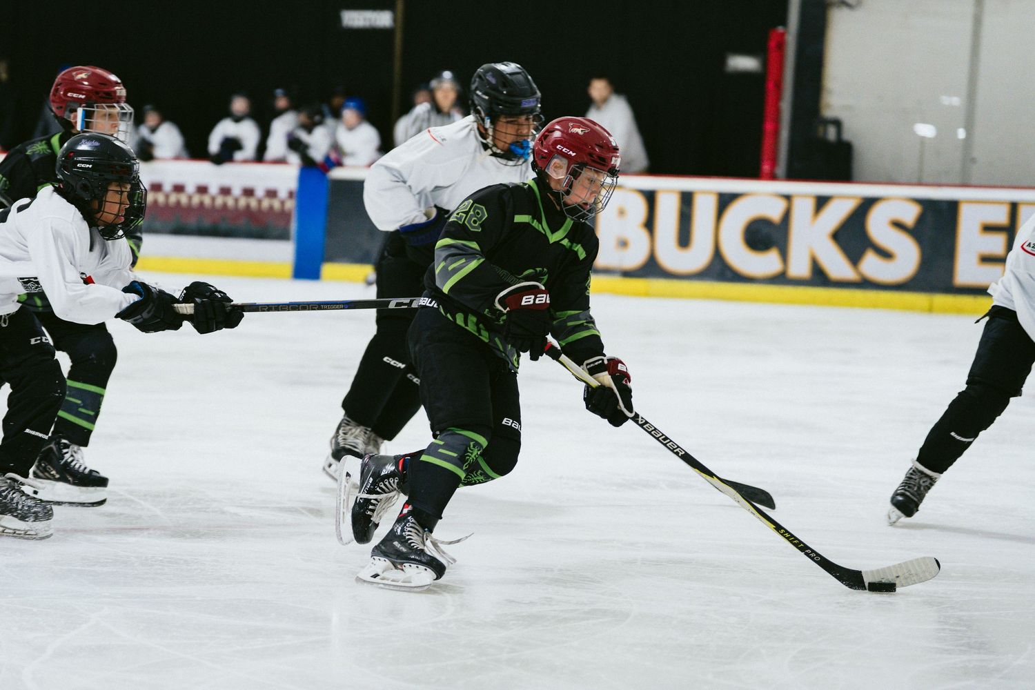 Youth ice hockey players in black uniforms skate and compete for the puck during an indoor game.
