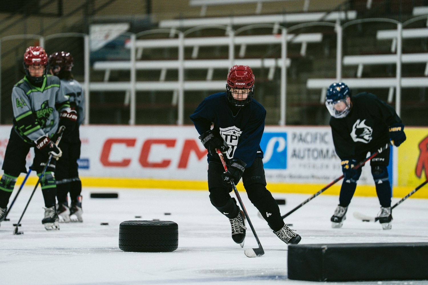 Three youth hockey players competing for puck during ice hockey drill at indoor skating rink.