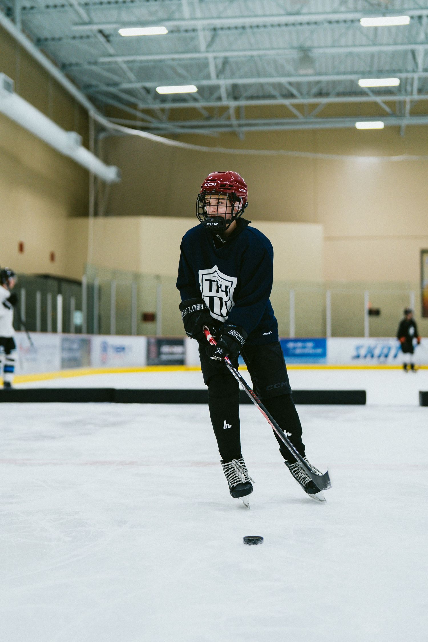 Young hockey player skating with puck during indoor ice hockey practice at a rink.