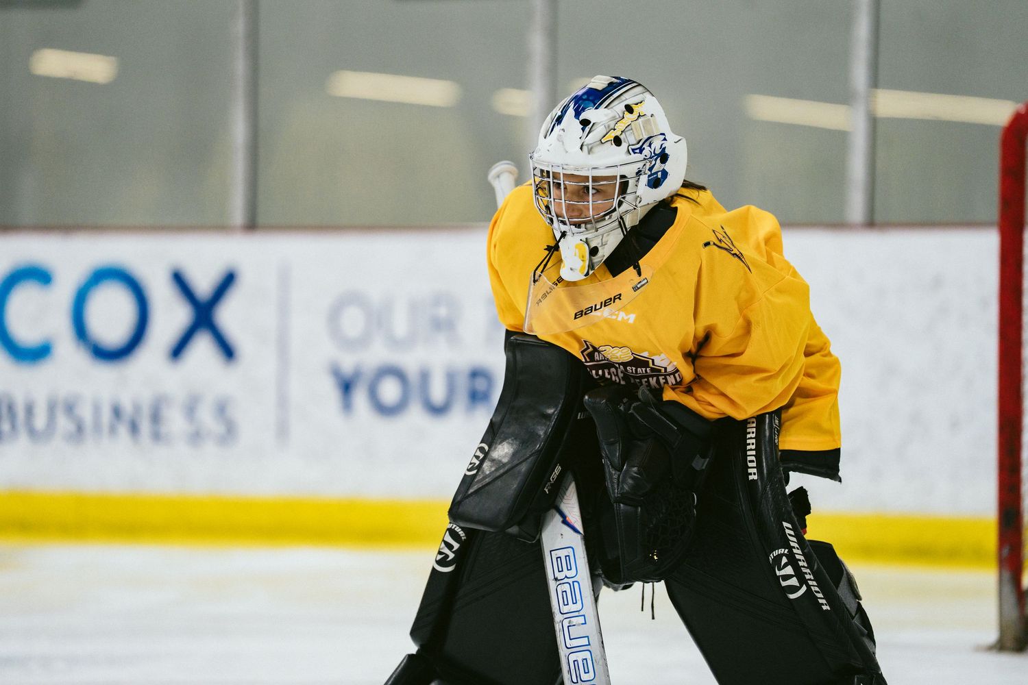 A youth ice hockey goalie in yellow gear practices in net during an indoor rink training session.