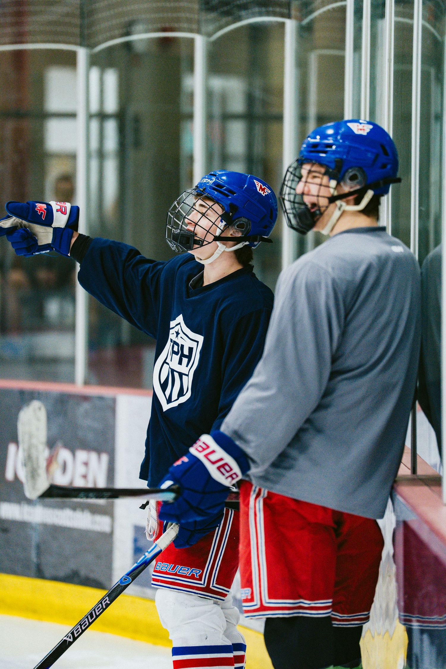 Young hockey players in blue TPH jerseys and helmets chat on the ice during practice at an indoor rink.