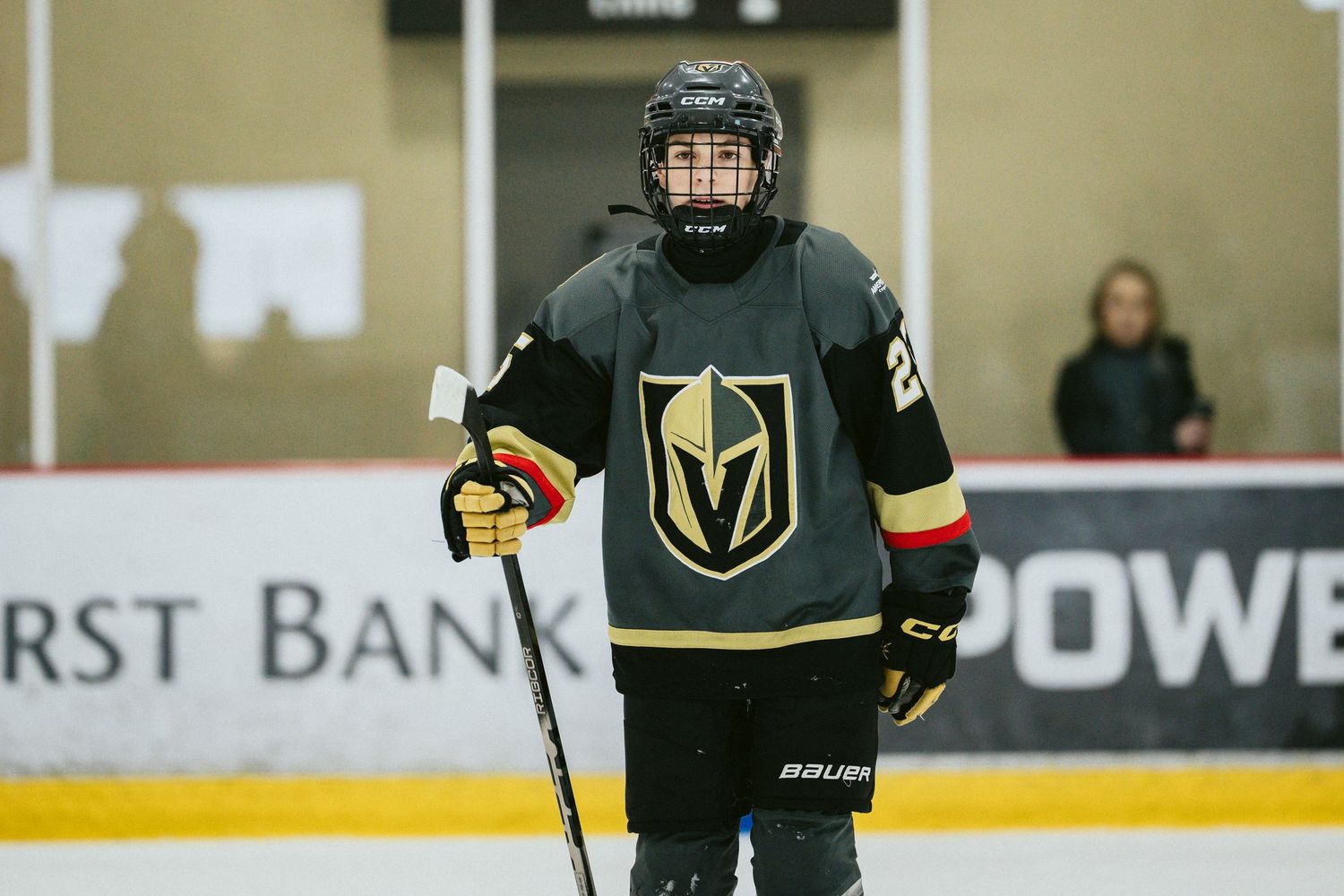 Youth hockey player in black and gold Vegas Knights uniform stands on ice.
