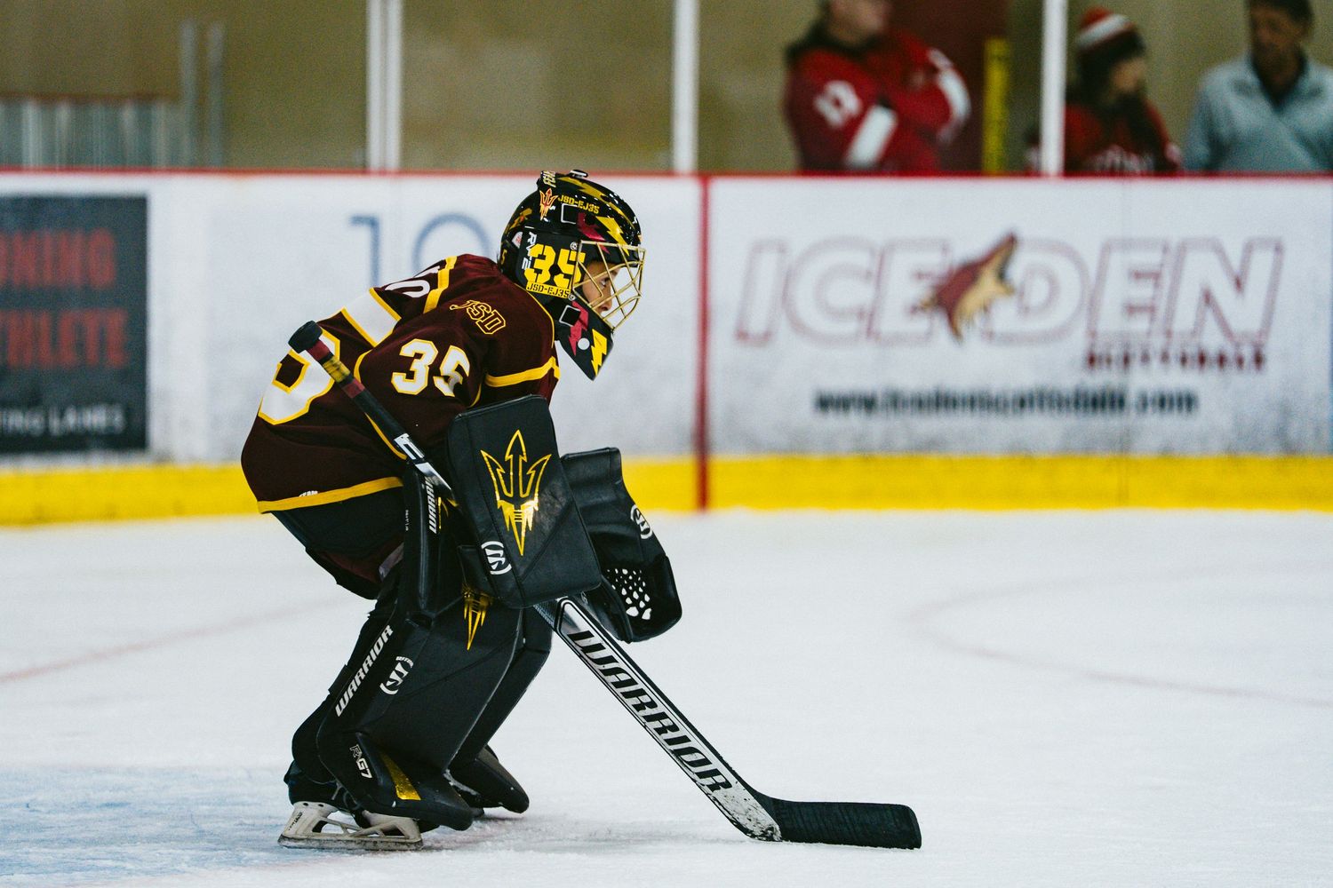 Hockey goalie in brown and gold uniform crouches in defensive position on the ice.