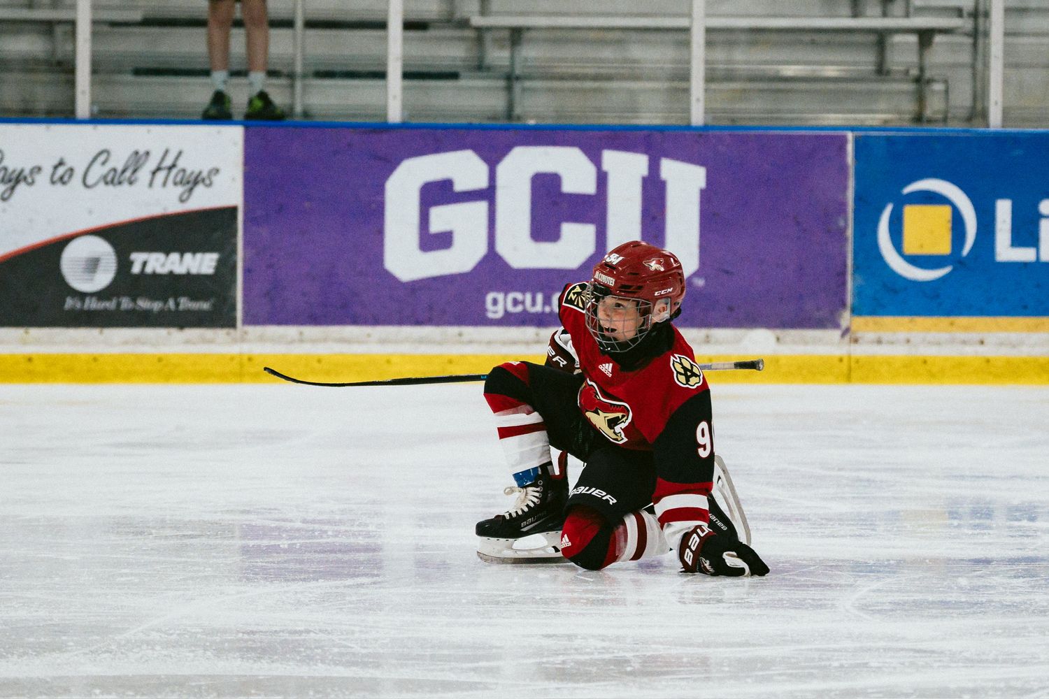 Hockey player in red jersey slides across the ice during intense game action.