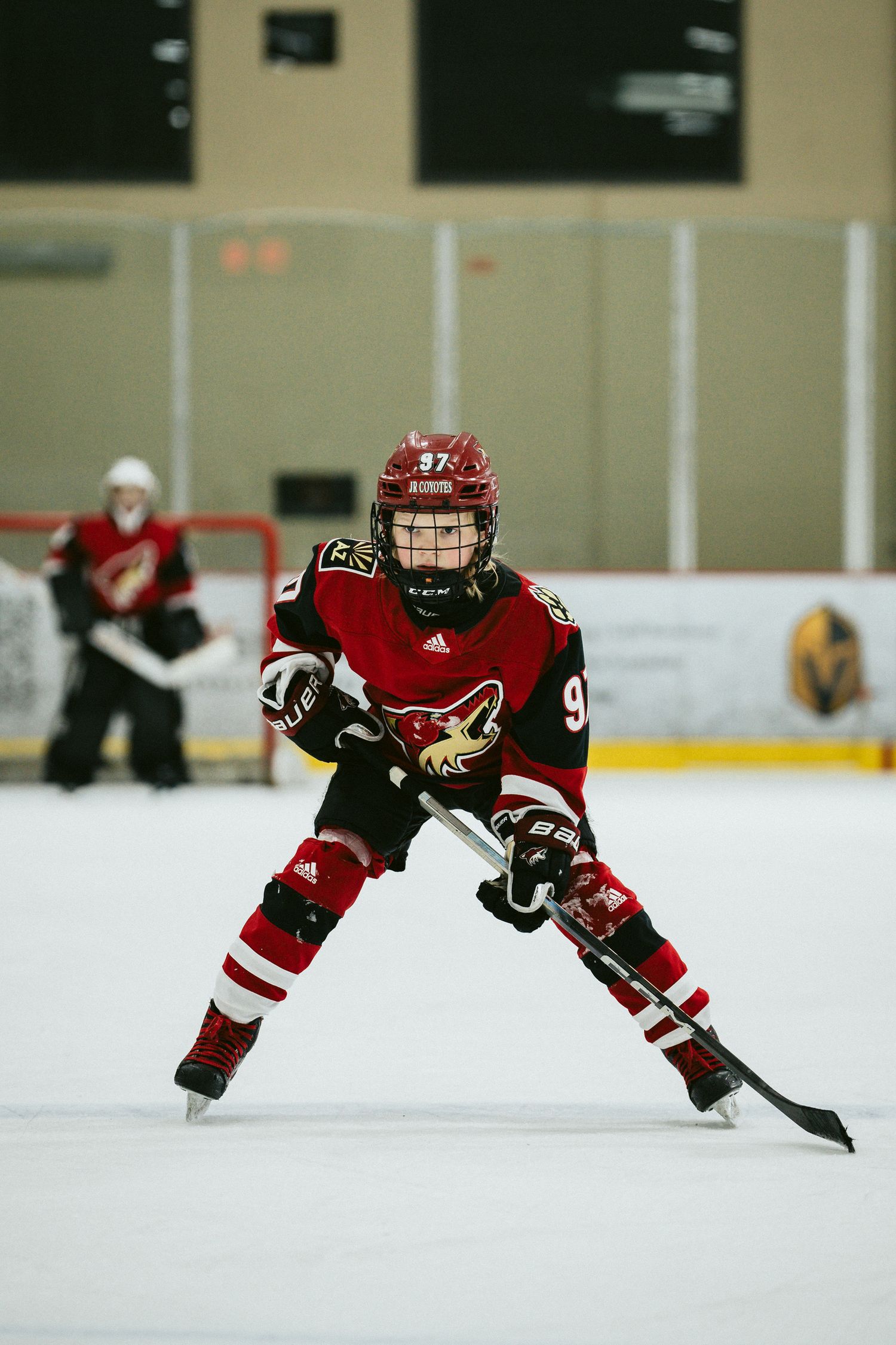 Youth hockey player in red jersey skating with stick during practice on ice rink.