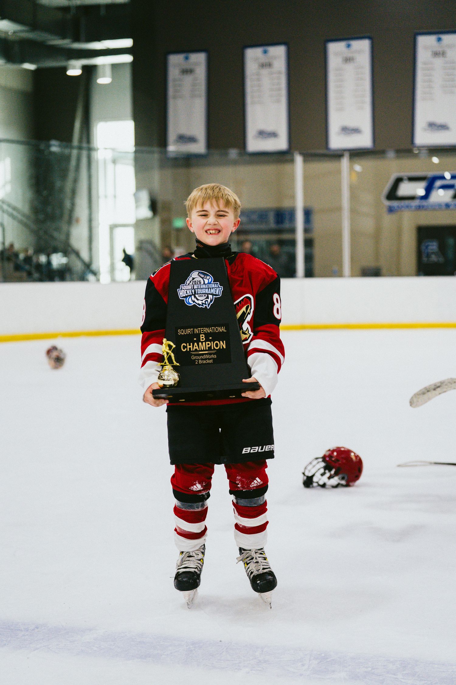 Young hockey player celebrating with championship trophy on indoor ice rink.