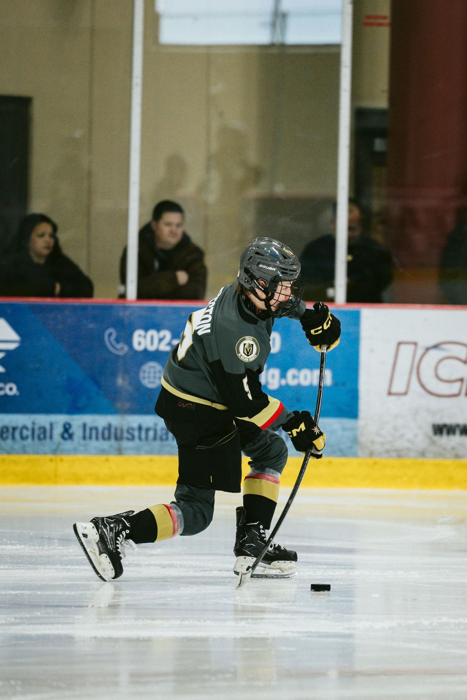 Hockey player in black uniform handles the puck while skating during a game.