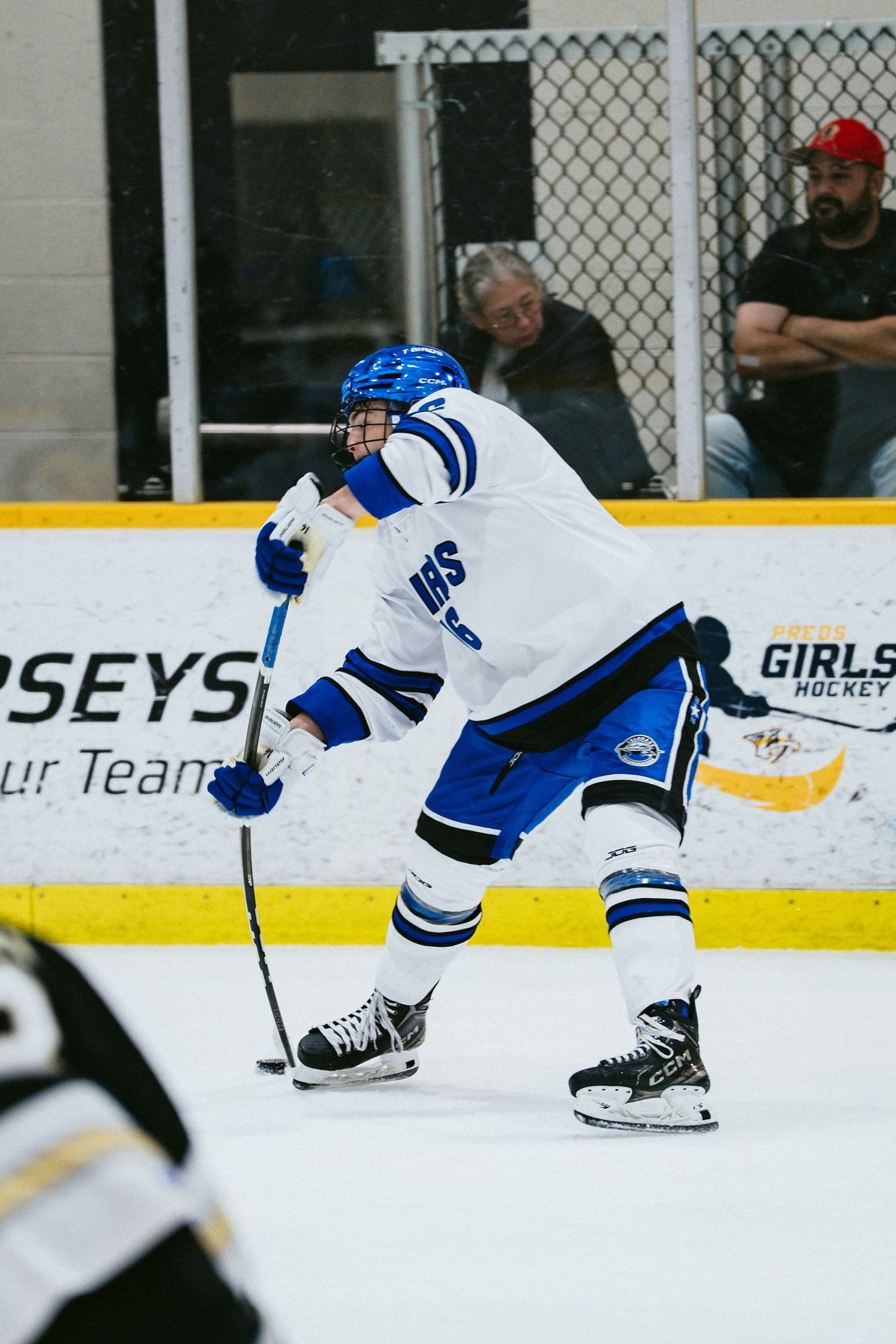 Hockey player in blue and white jersey takes a shot on ice during a competitive game.