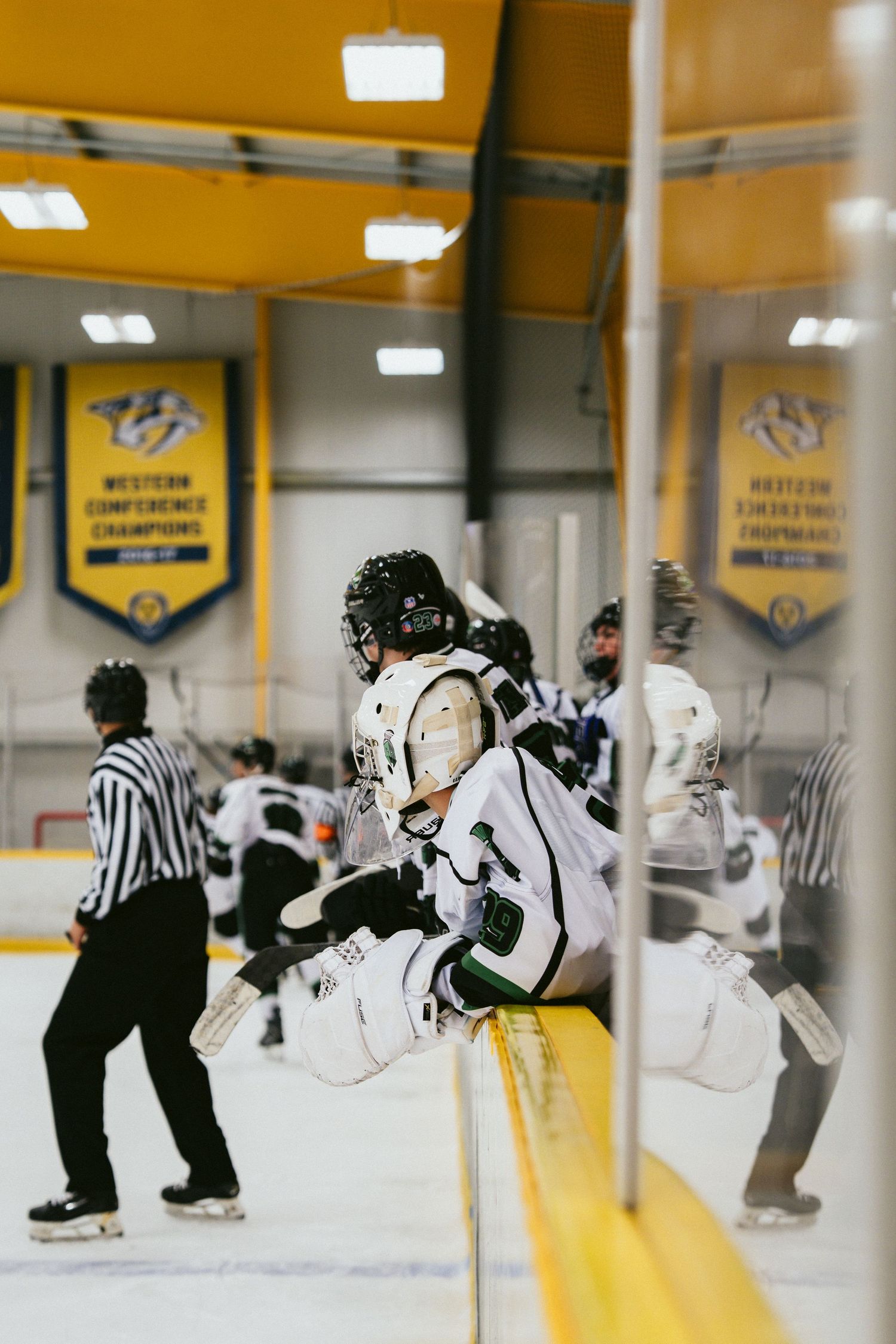Young hockey players on ice rink bench during game, with Nashville Predators Western Conference Champions banners in background.